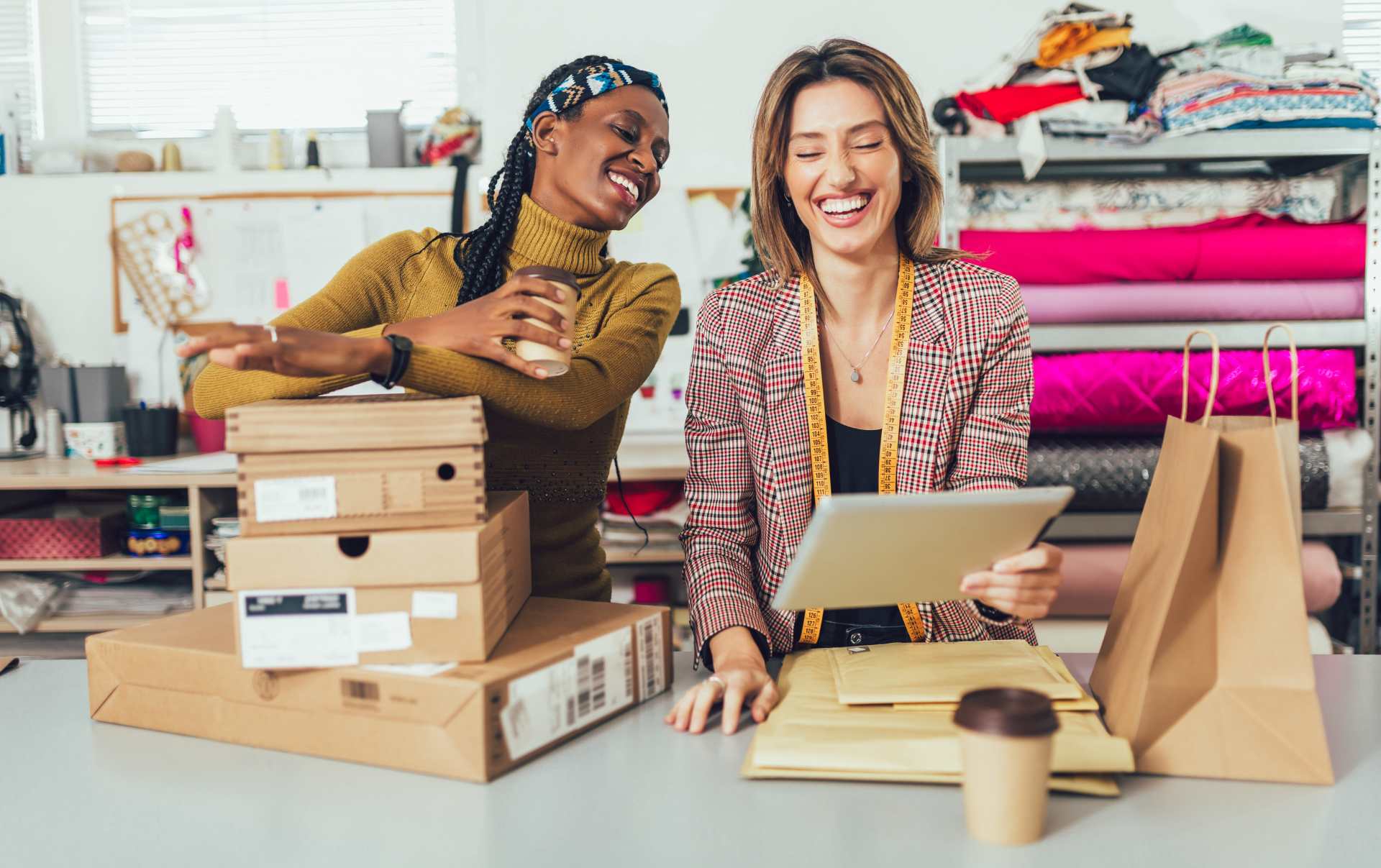 Two businesswoman smiling joyfully at their tablet as their ecommerce website conversion rates increase while they pack orders