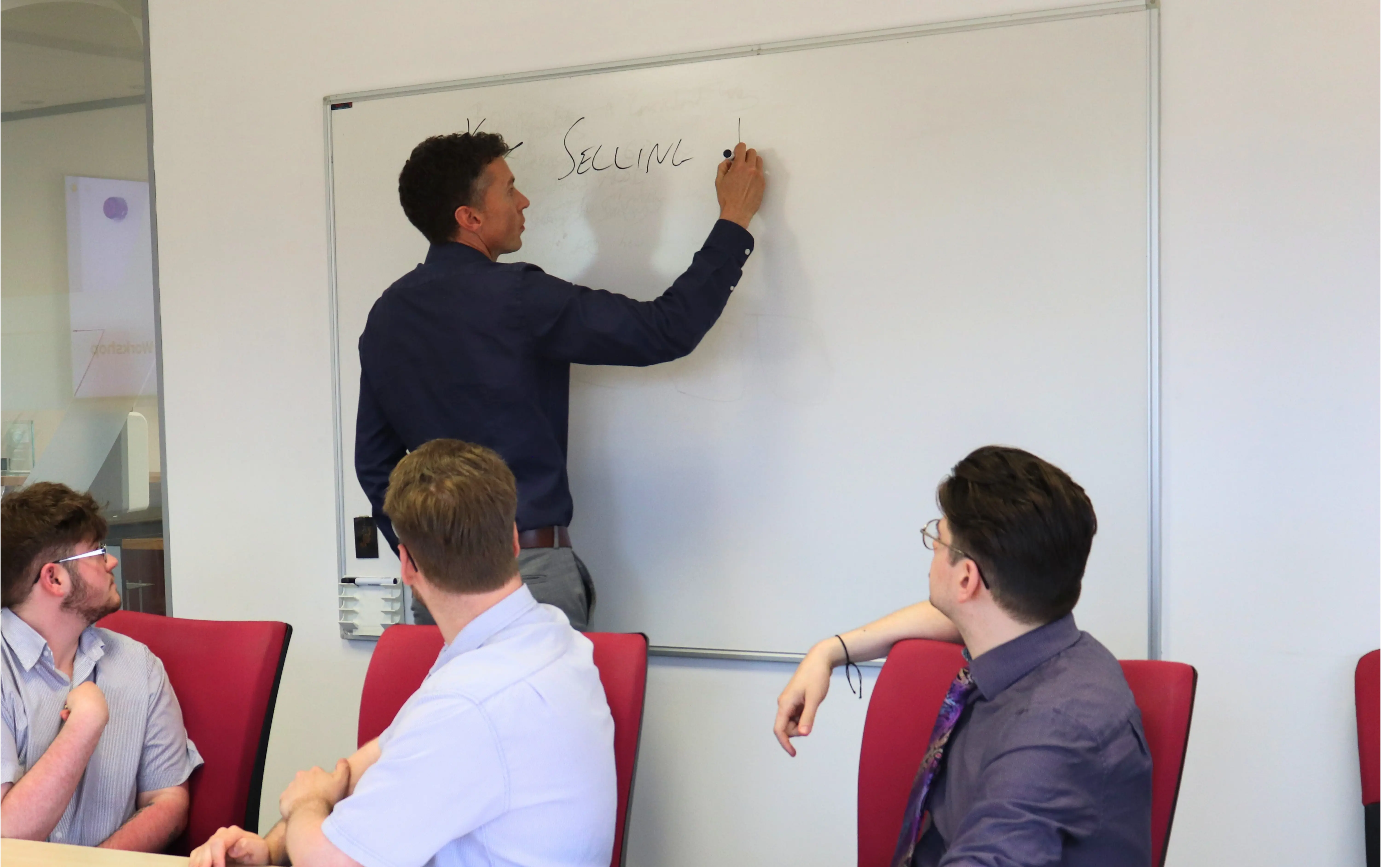 Will from JDR writing on a whiteboard during a training session while colleagues watch and take part in the discussion.