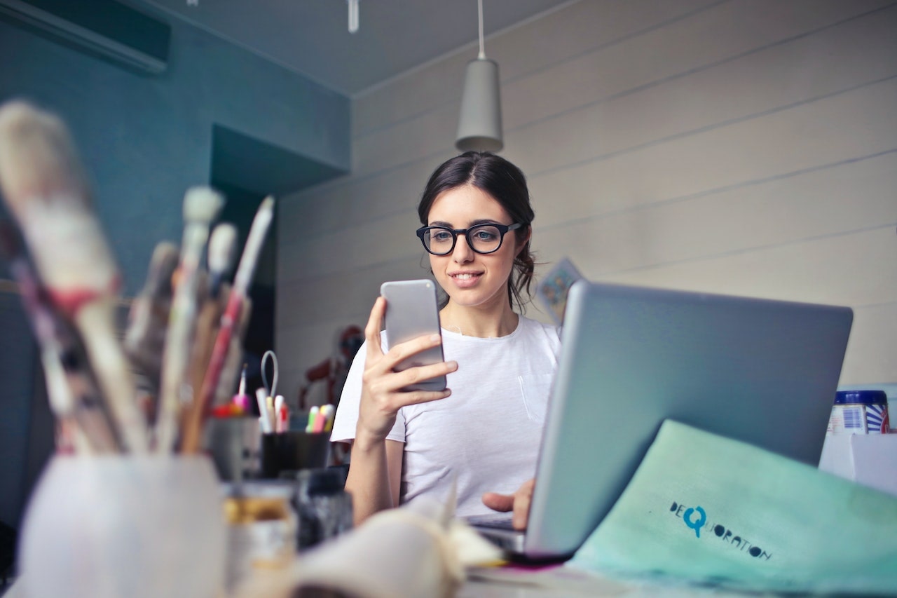 A business owner sitting at her cluttered desk, looking at her phone to see her marketing automation progress