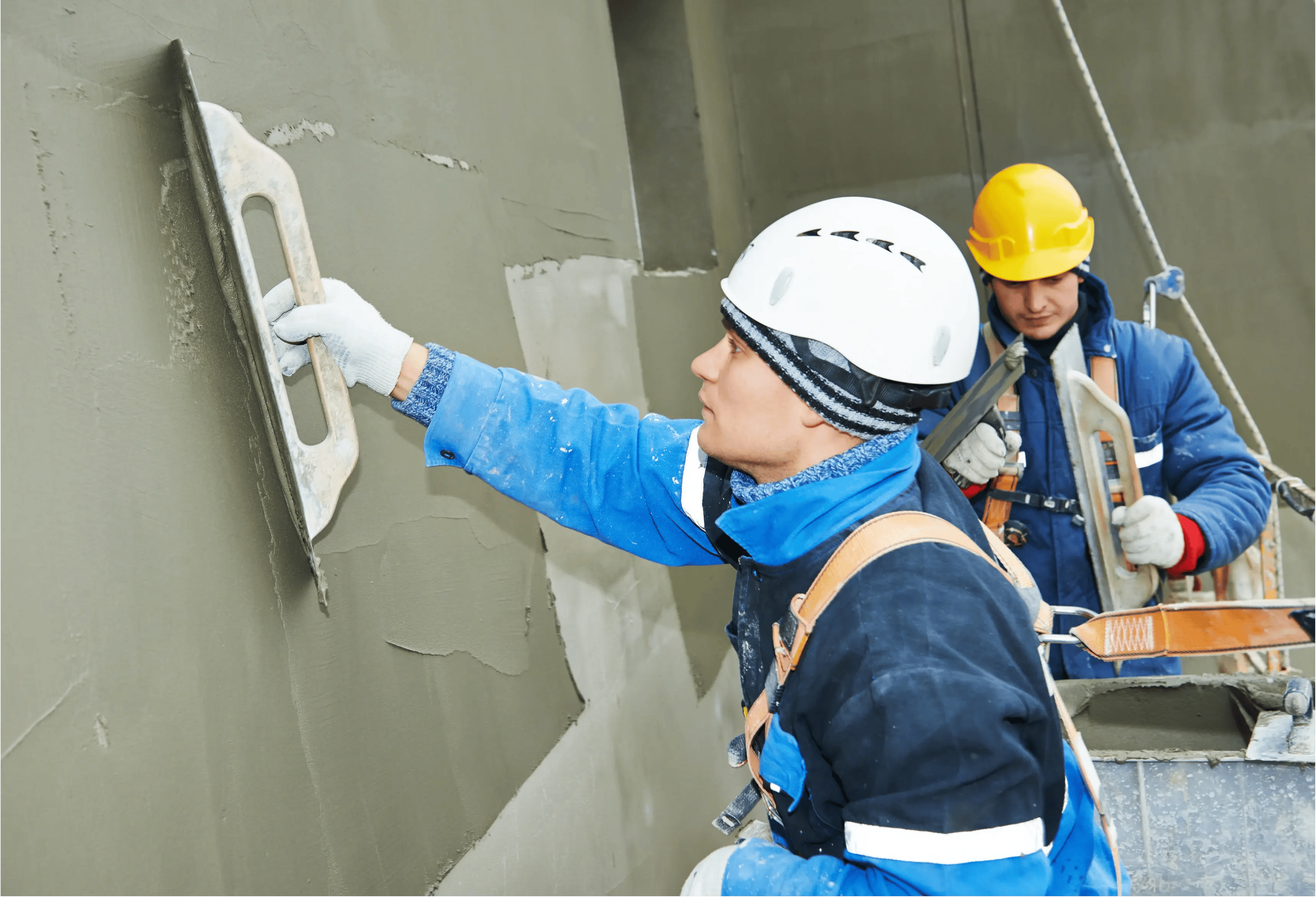 Two construction workers applying plaster to a wall with trowels.