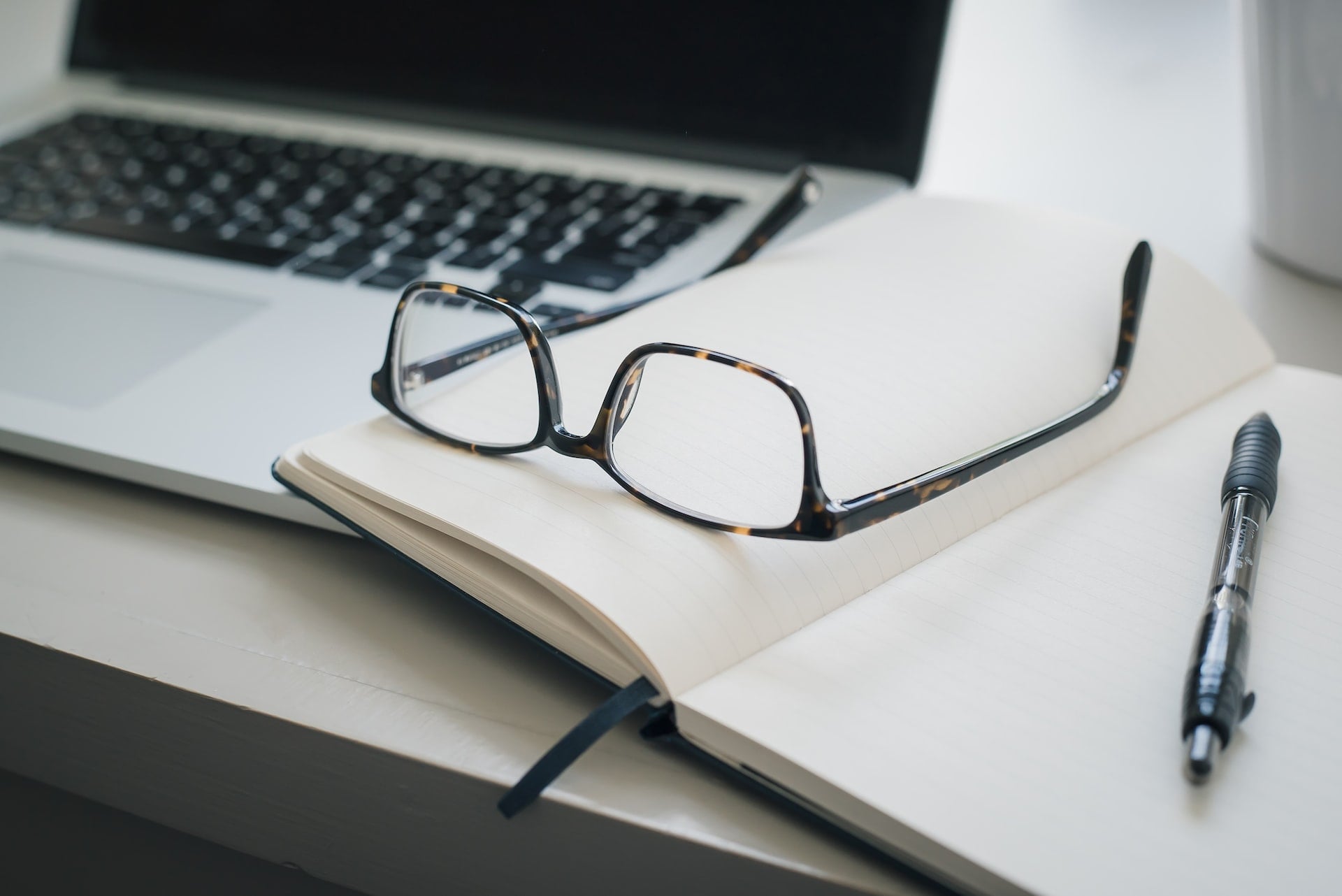 A business owner's glasses on their notebook resting on a laptop as they plan content to help grow their business