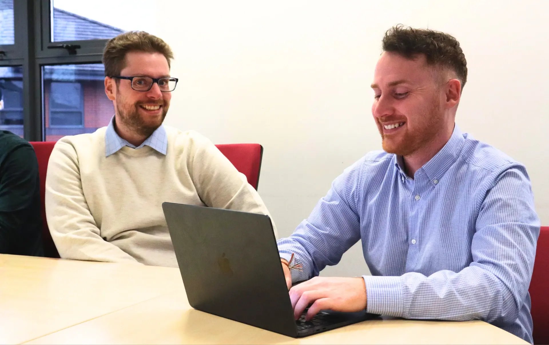 Rhys and John reviewing SEO performance data on a laptop during a strategy meeting about Google AI Overviews and website traffic growth.