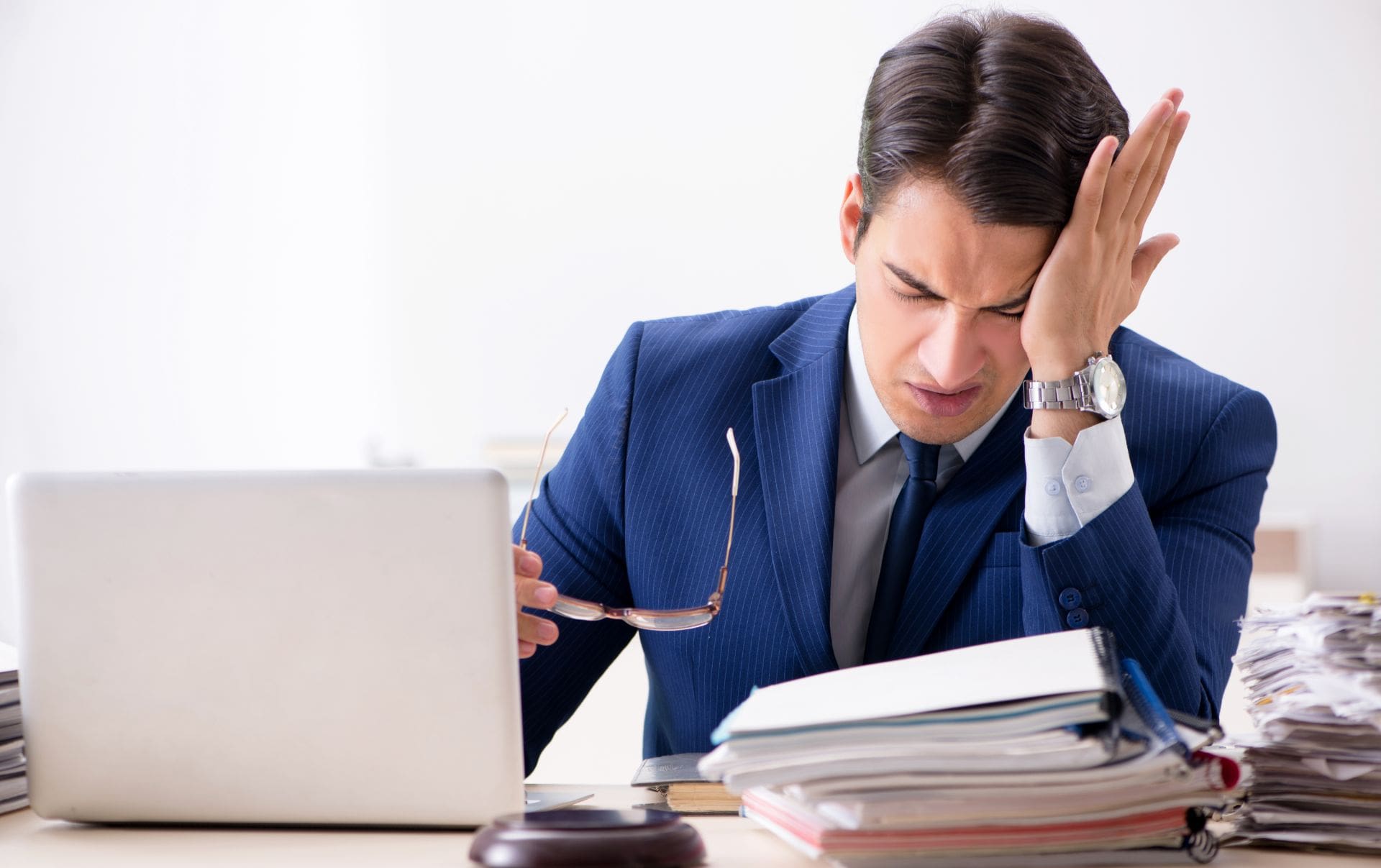A business owner rubbing his head in frustration from the pile up of work on his desk next to his laptop wanting a easier way to navigate his workload and personal life. 