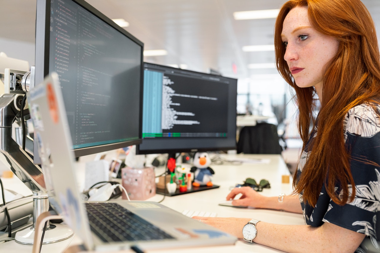 A woman working on two PC screens and a laptop in an engineering company which is successfully gaining customers from an effective website