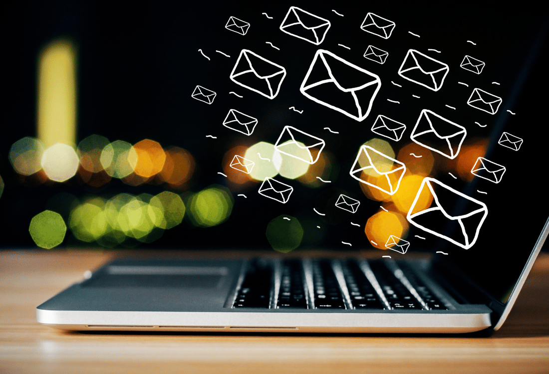 A laptop on a table with email icons floating above.