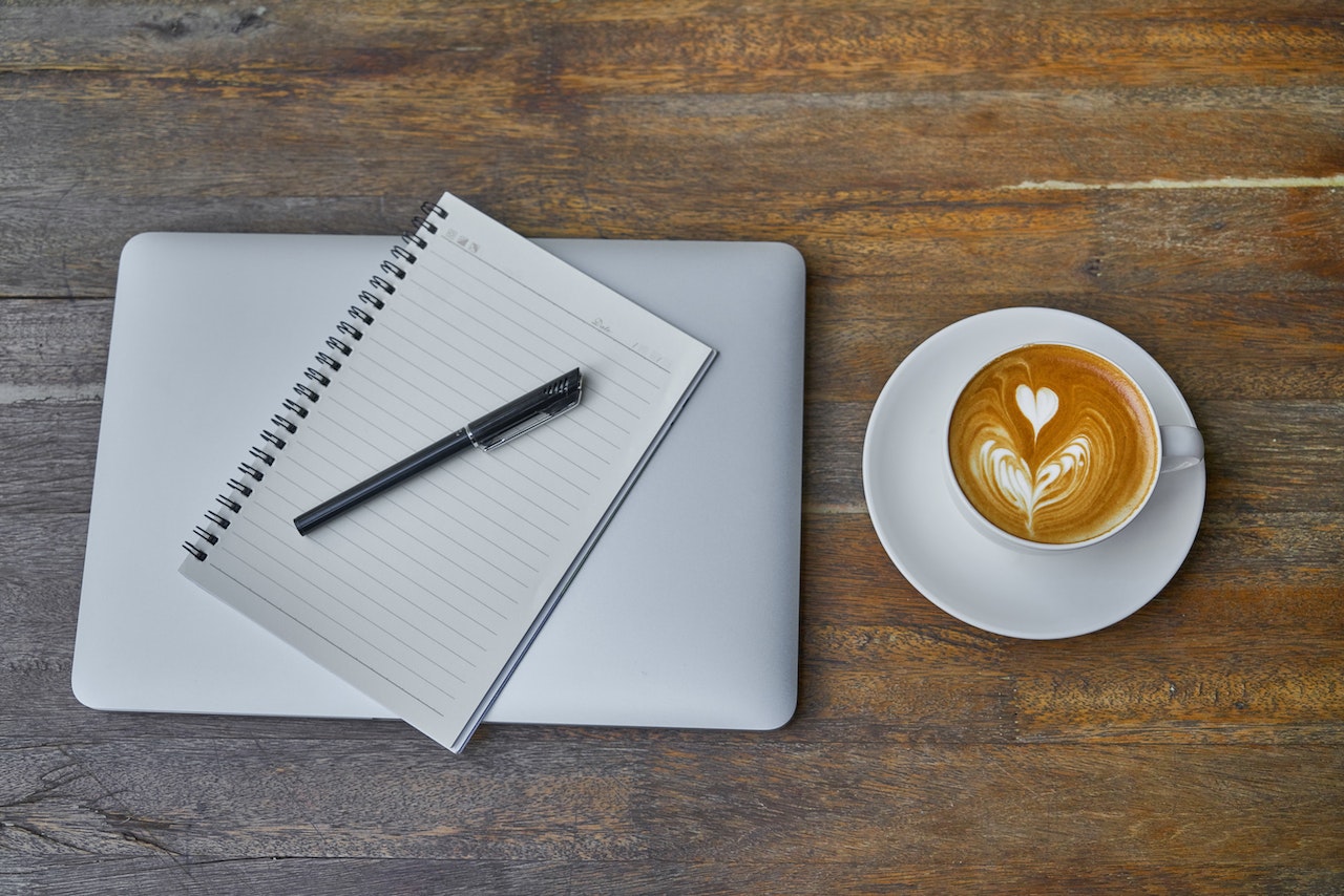 A notebook and pen laying on a laptop next to a latte ready to be used for brainstorming lead generating content ideas.