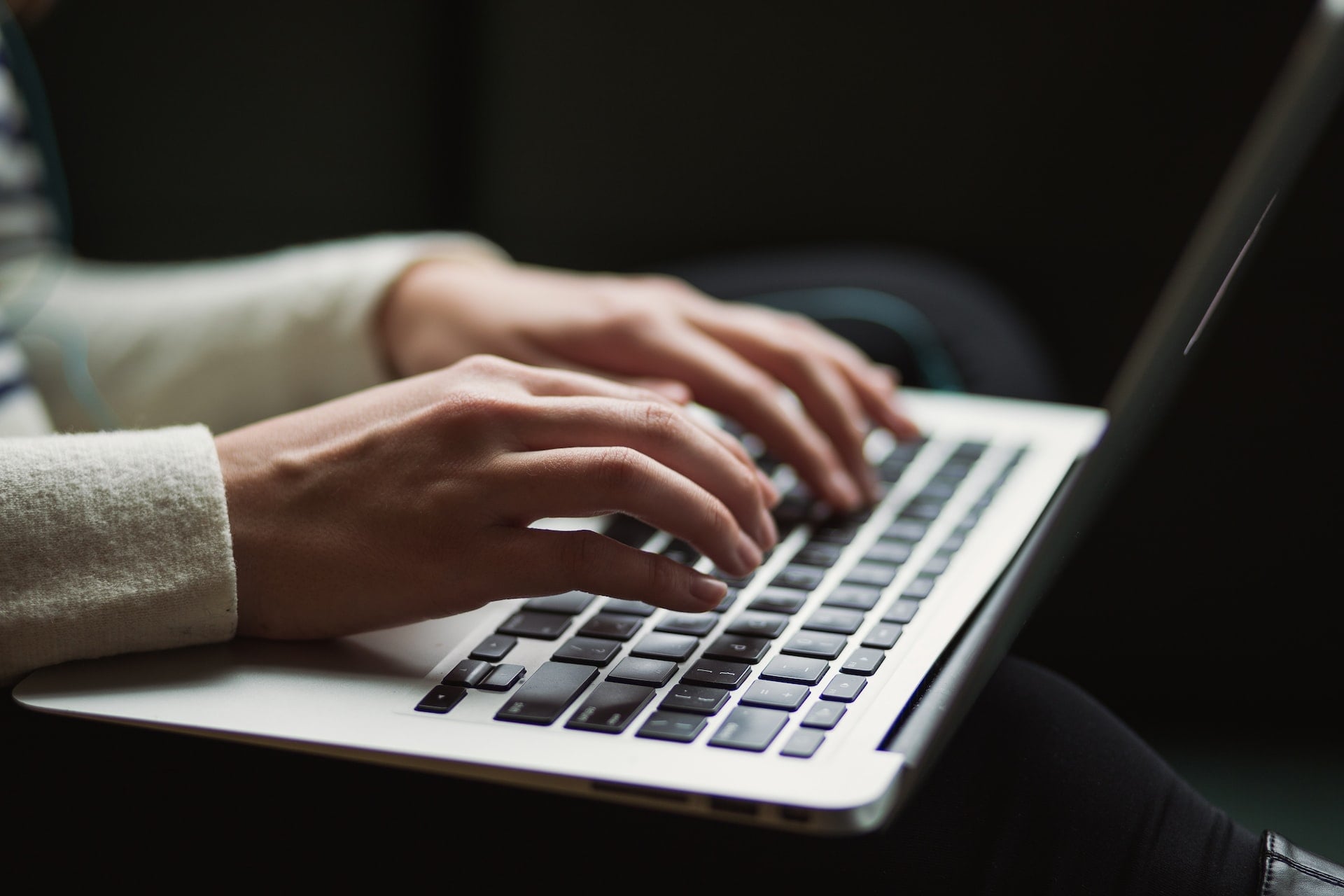 A businesswoman writing with her laptop on her knees, finding a consistent tone of voice for her business's content marketing strategy