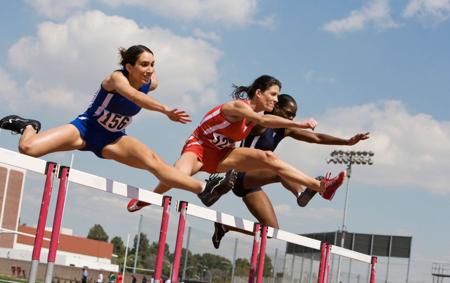 Three business women running a race with hurdles mid-jump as they scale over sales hurdles in their S M E to help with business growth