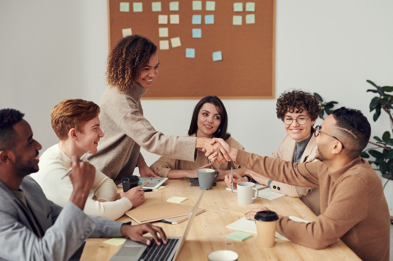 A sales team meeting around a conference table, two of them shaking hands across the table as they survive and thrive in the recession