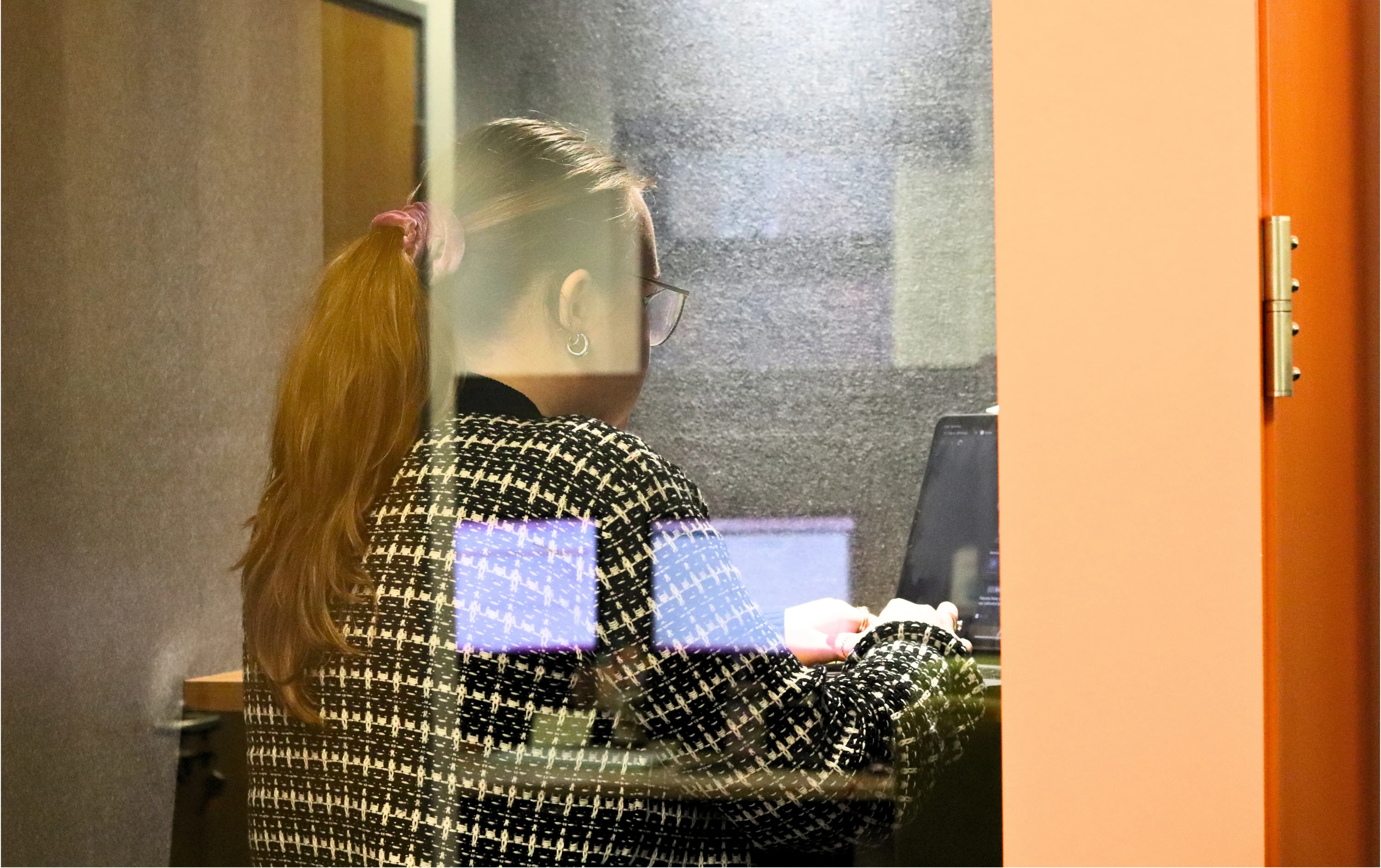 Ellis from JDR working on a laptop inside a quiet office booth, viewed through the glass panel.