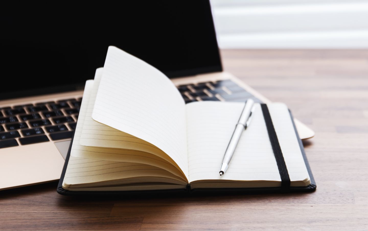 A notebook resting open on the keyboard of a laptop with a pen about to be written in by a business owner refining their content strategy to use their business's existing content to get more leads