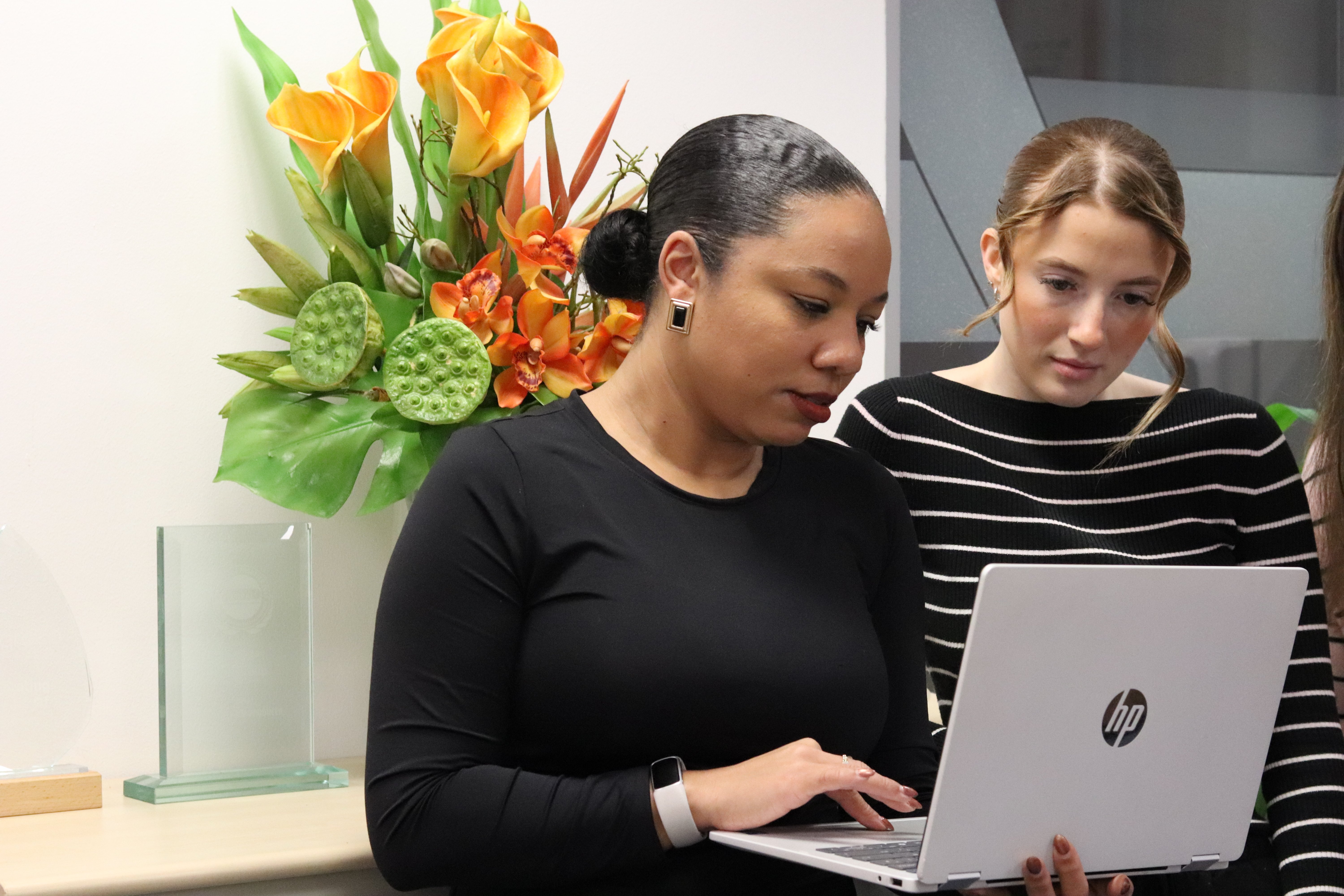 Kerry and Ellie gathered around a laptop that Kerry is holding, discussing social media marketing.