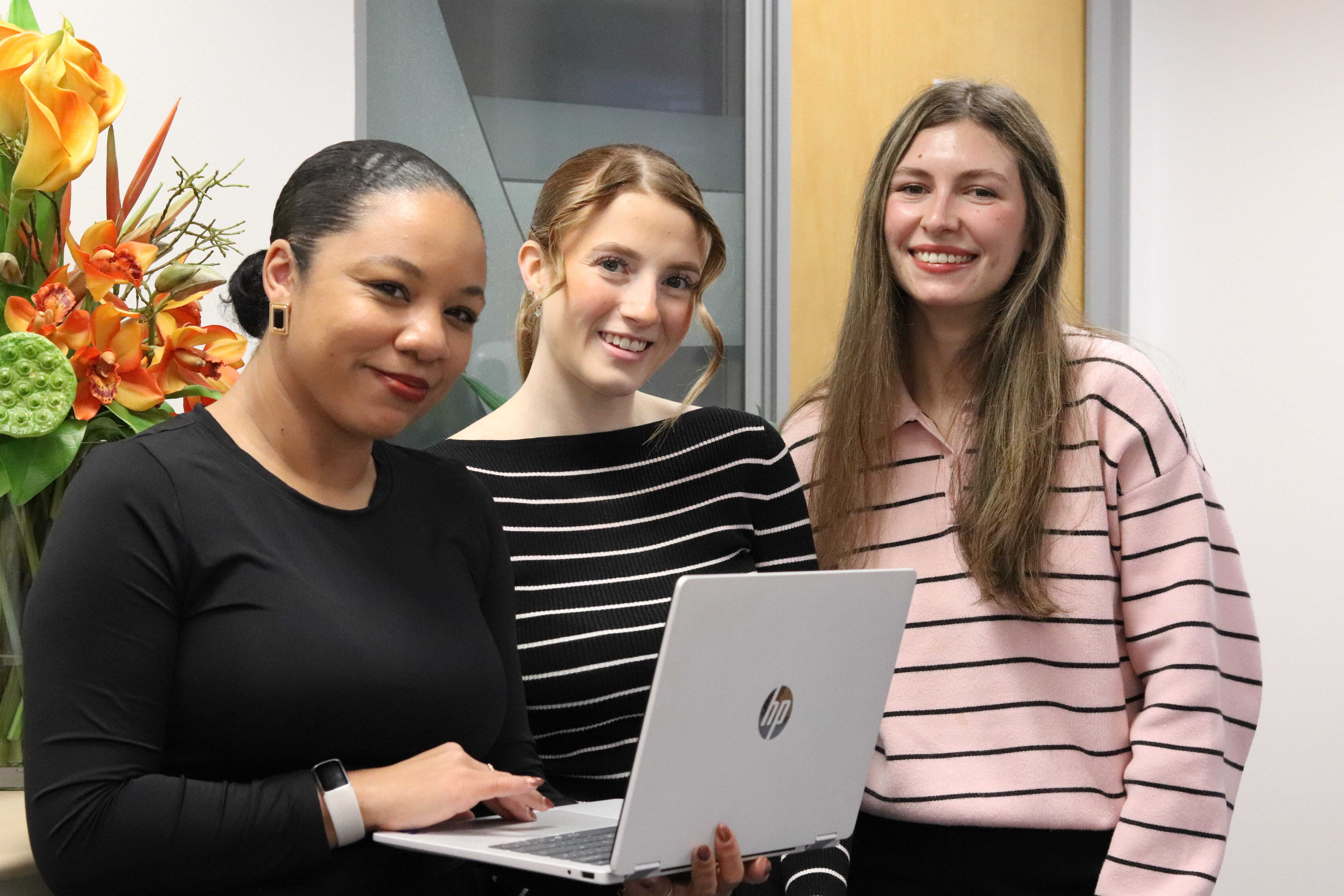 Kerry, Ellie, and Sophie smiling and looking at laptop which Kerry is holding.