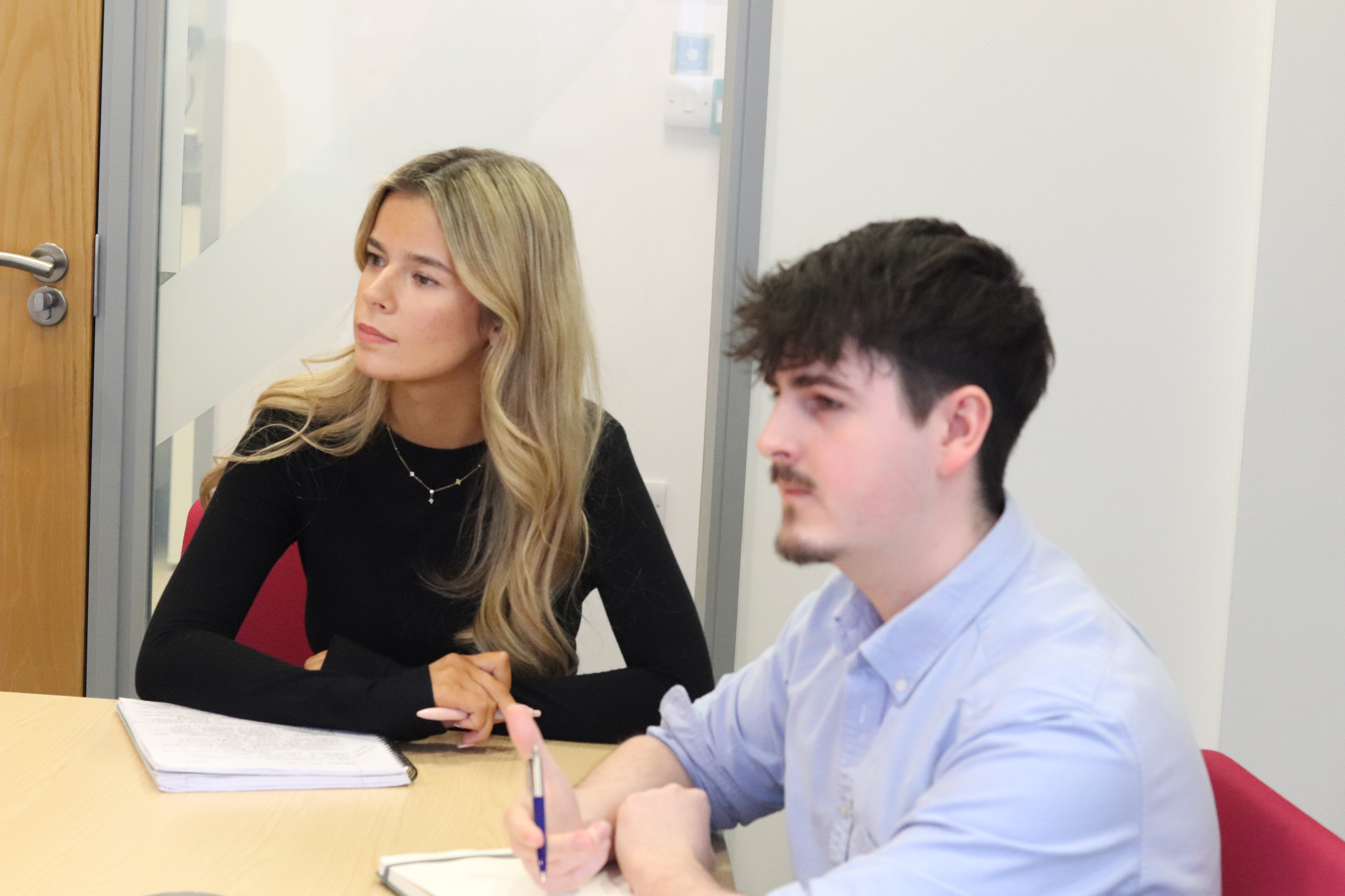 Mia and Harry with note books and pens focusing during a meeting.