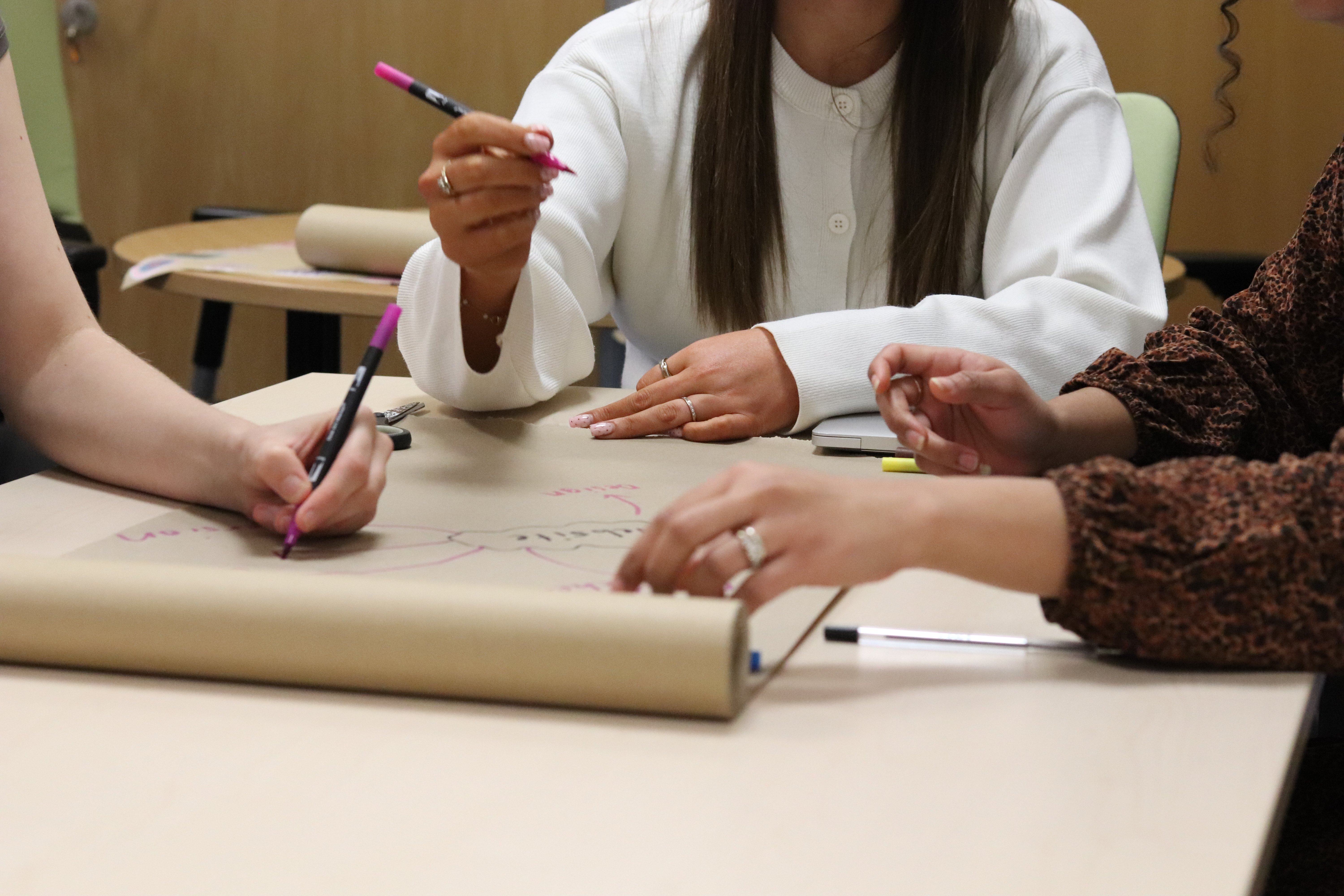 Emily and a few other team members gathered around a mindmap on a table wwith pens in their hands writing ideas for a website topic.