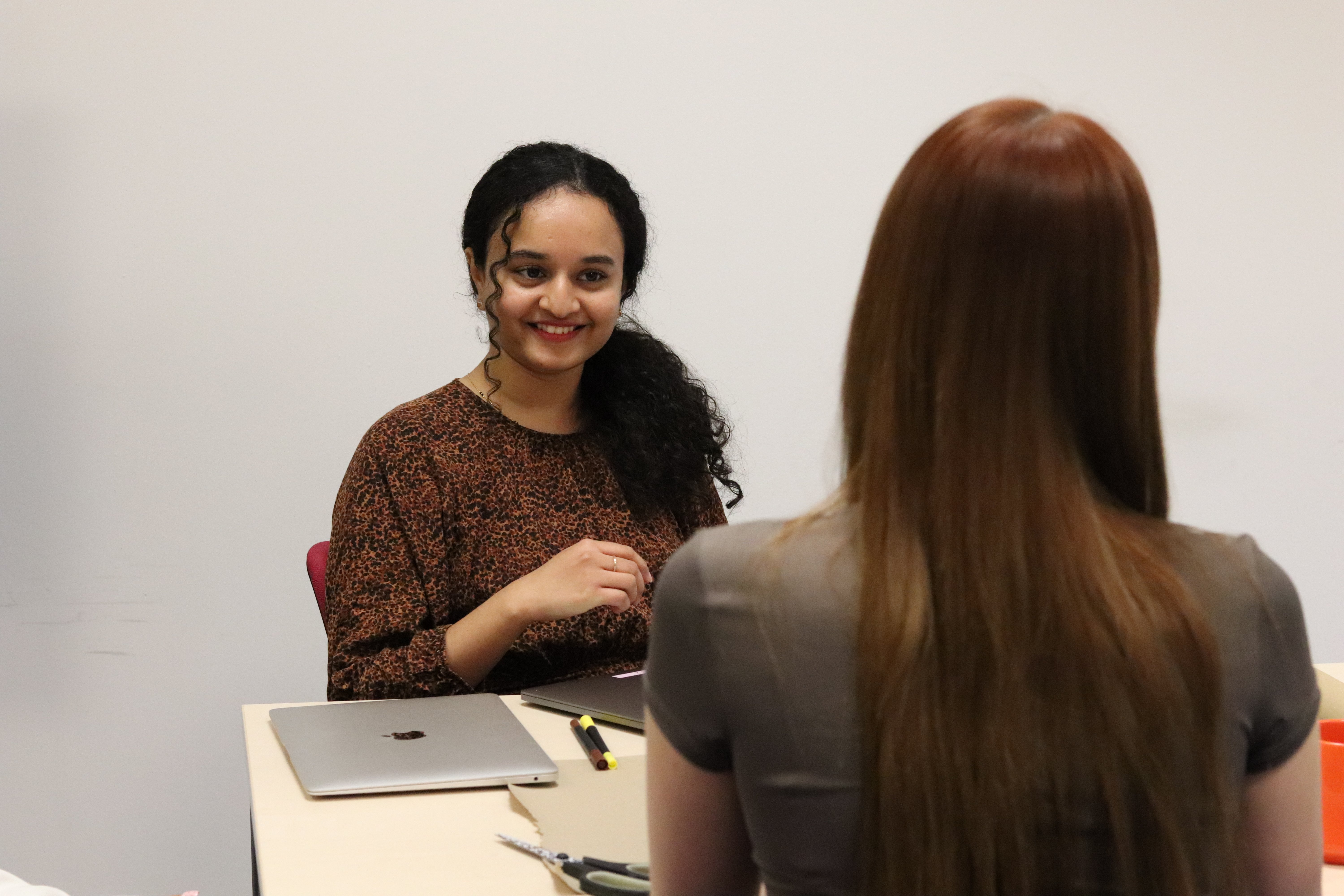 Ash with her laptop and pens smiling at Charlotte during a meeting.