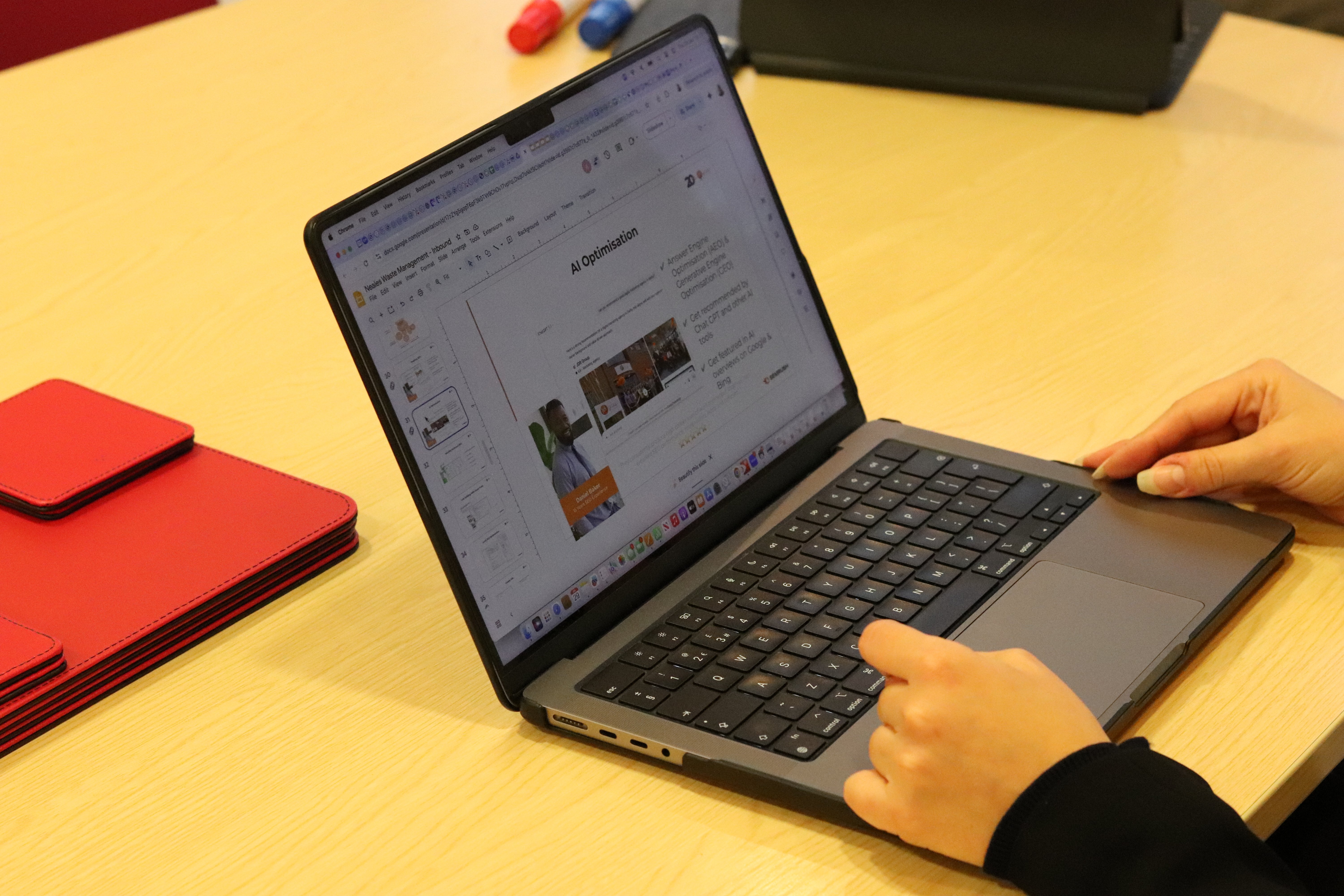 A laptop open with a hand typing on it, with the screen displaying a powerpoint slide on AI optimisation.