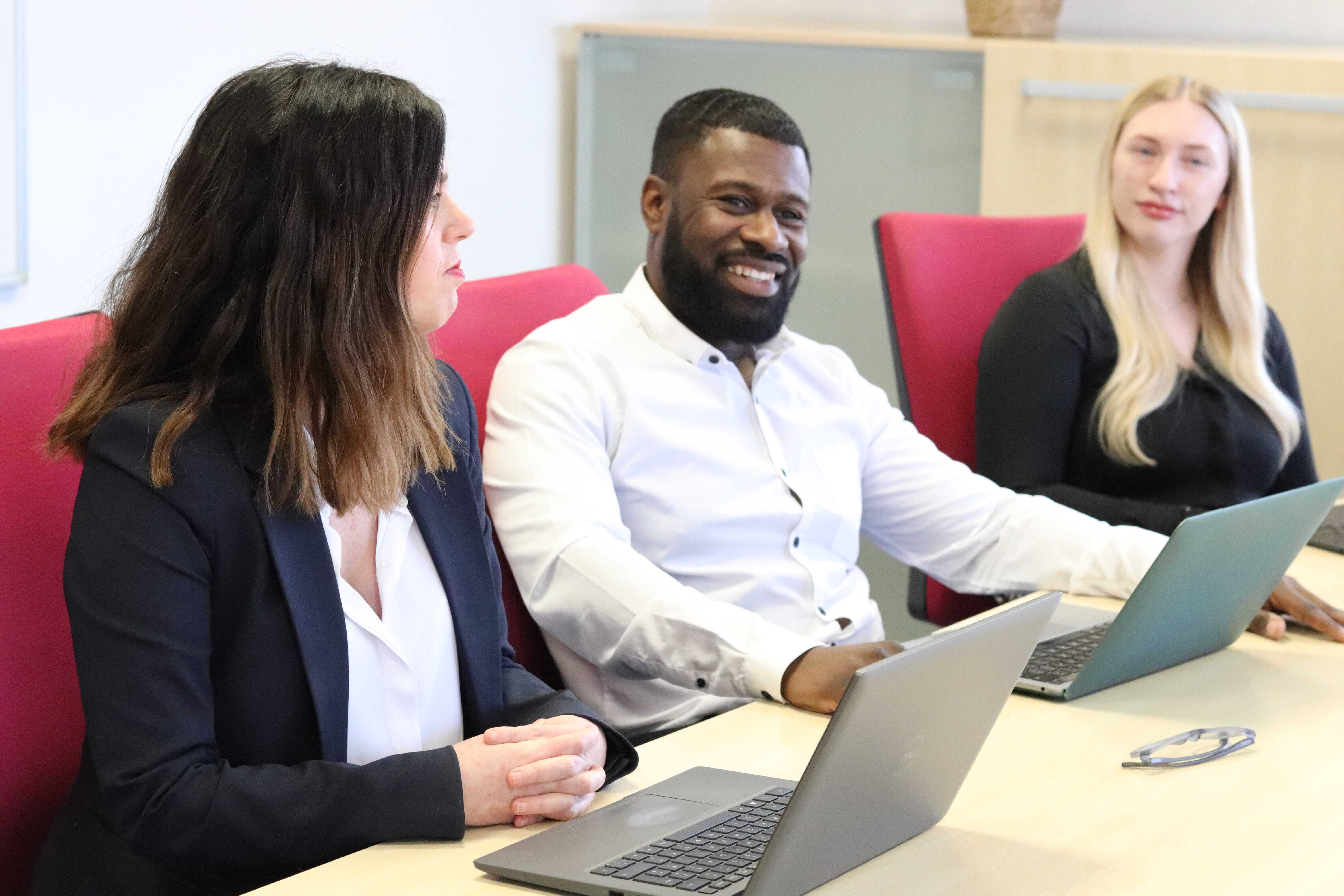 Shirley, Dan and Amber smiling in a meeting with laptops in front of them, discussing how to manage a business downturn.