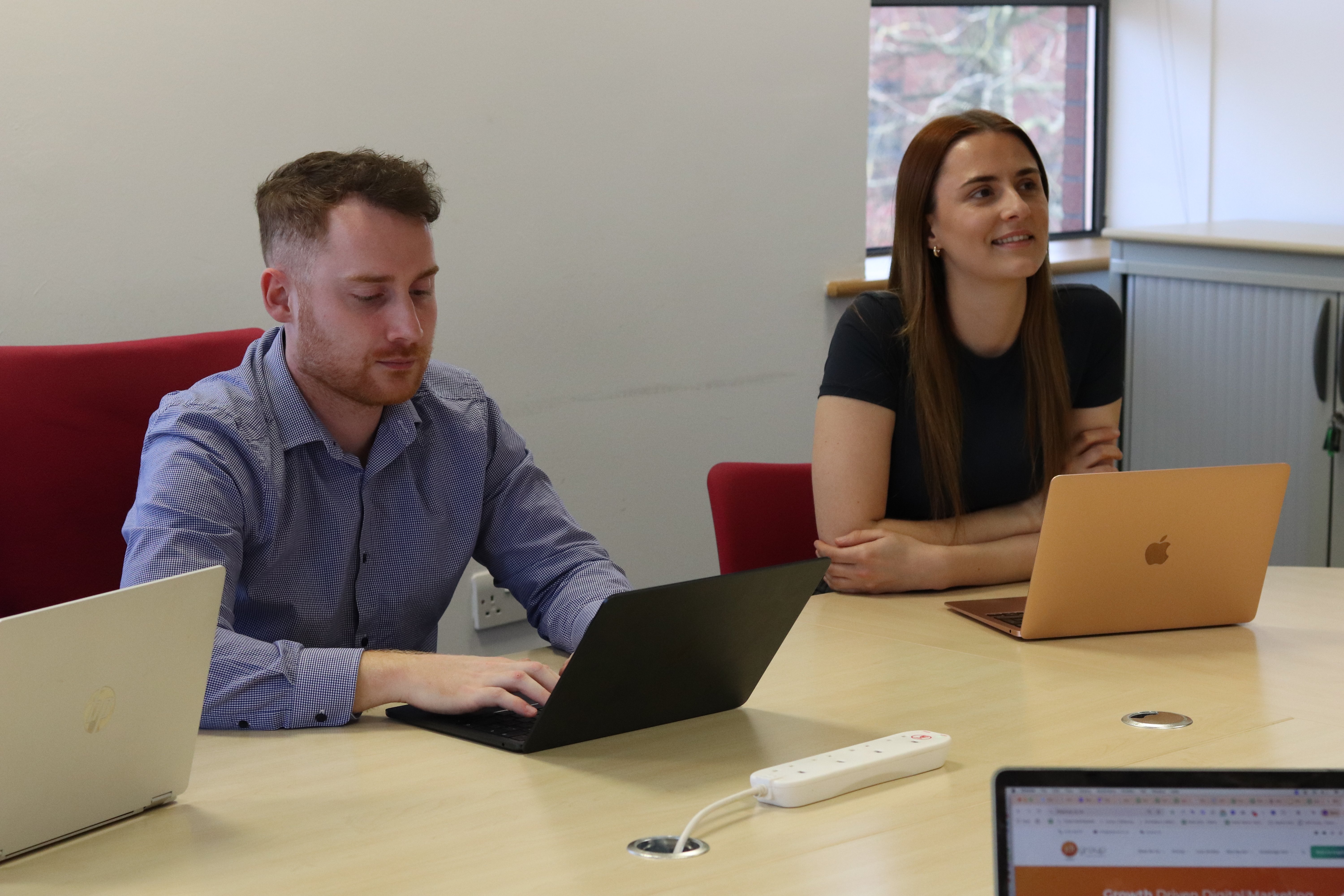John and Charlotte working on their laptops in a meeting.