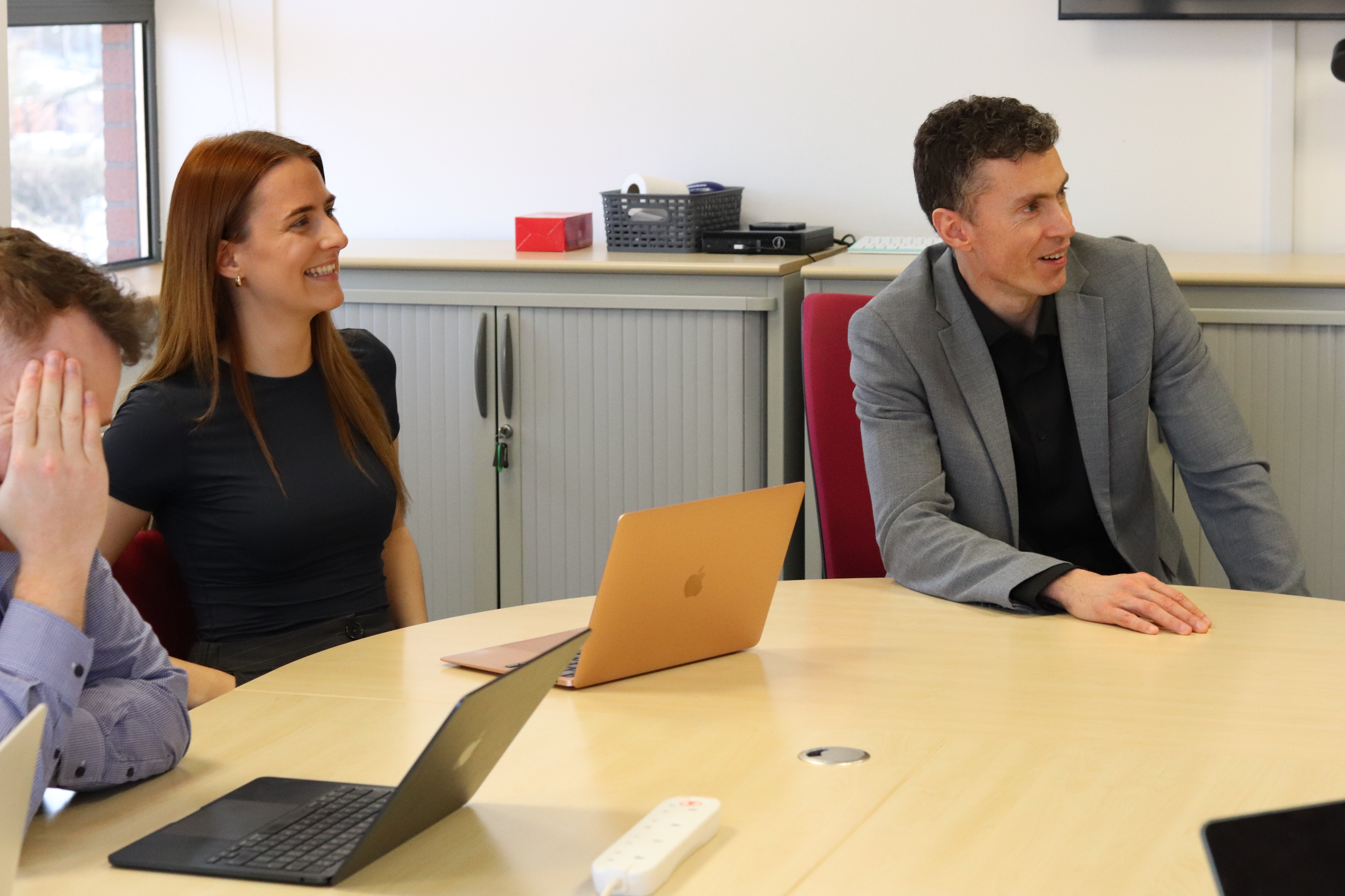 John, Charlotte, and Will with two laptops open engaging during a meeting about sales enablement.