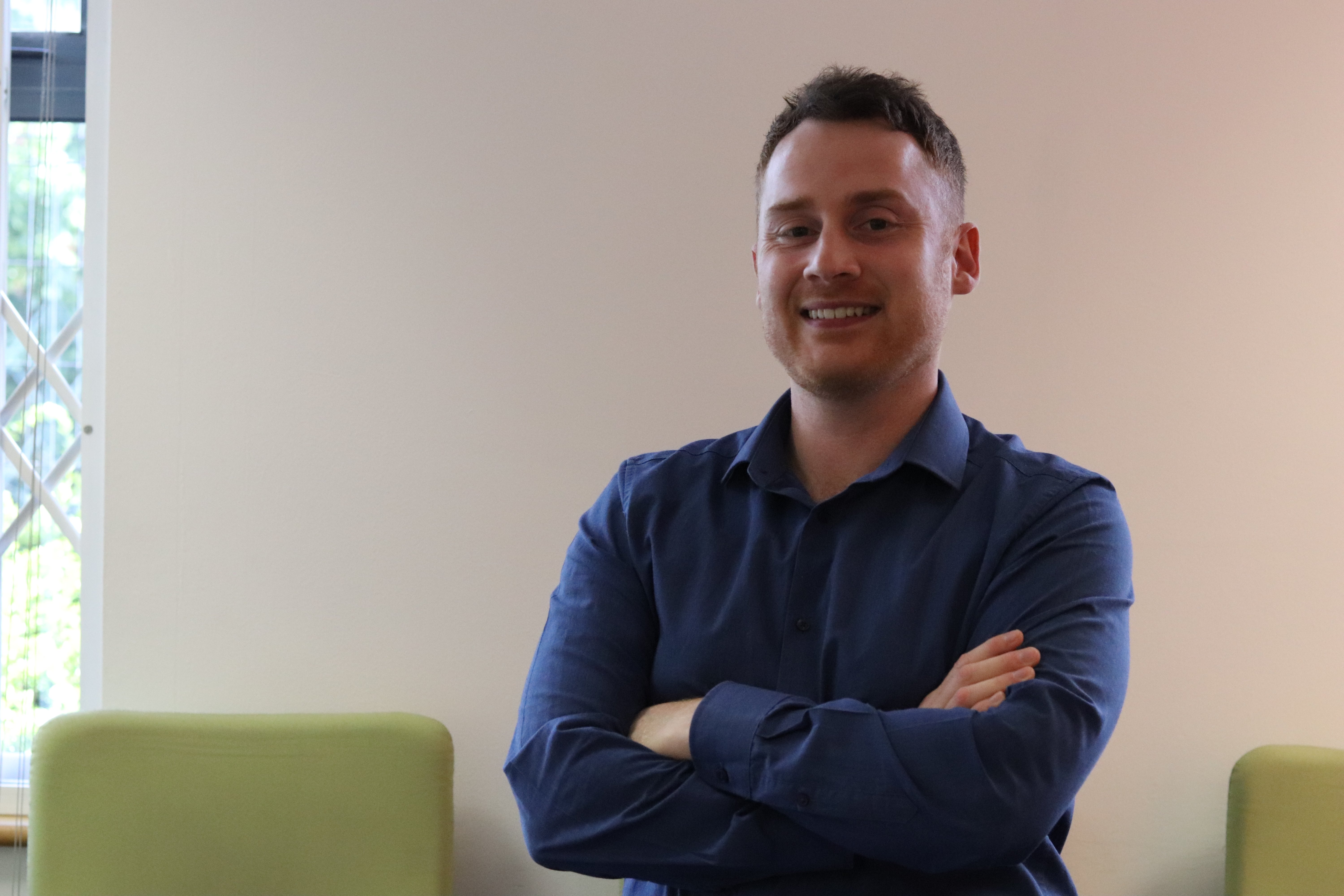 John with his arms crossed smiling at the camera in a meeting room.