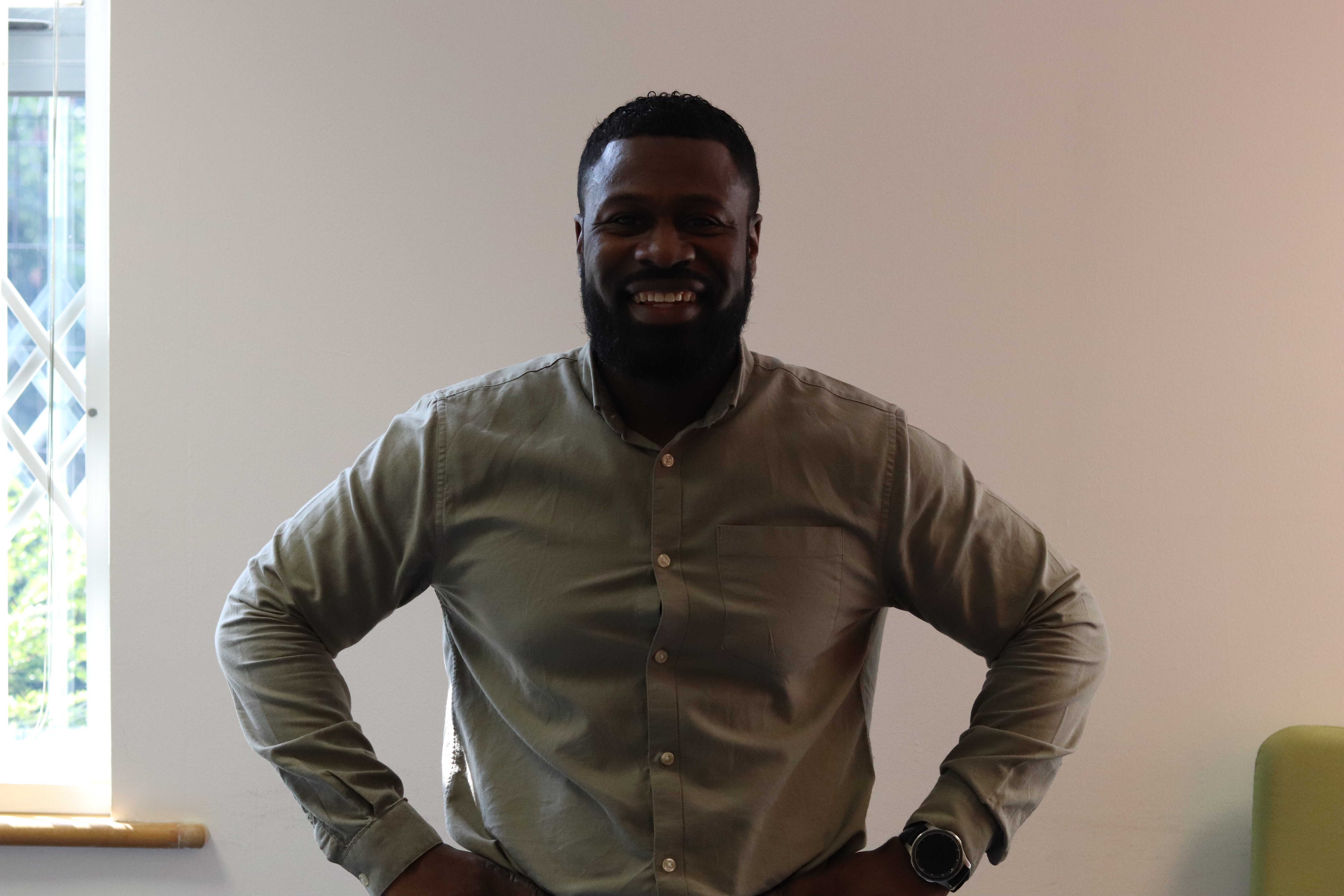 Dan with his hands on his hips smiling at the camera in a meeting room.