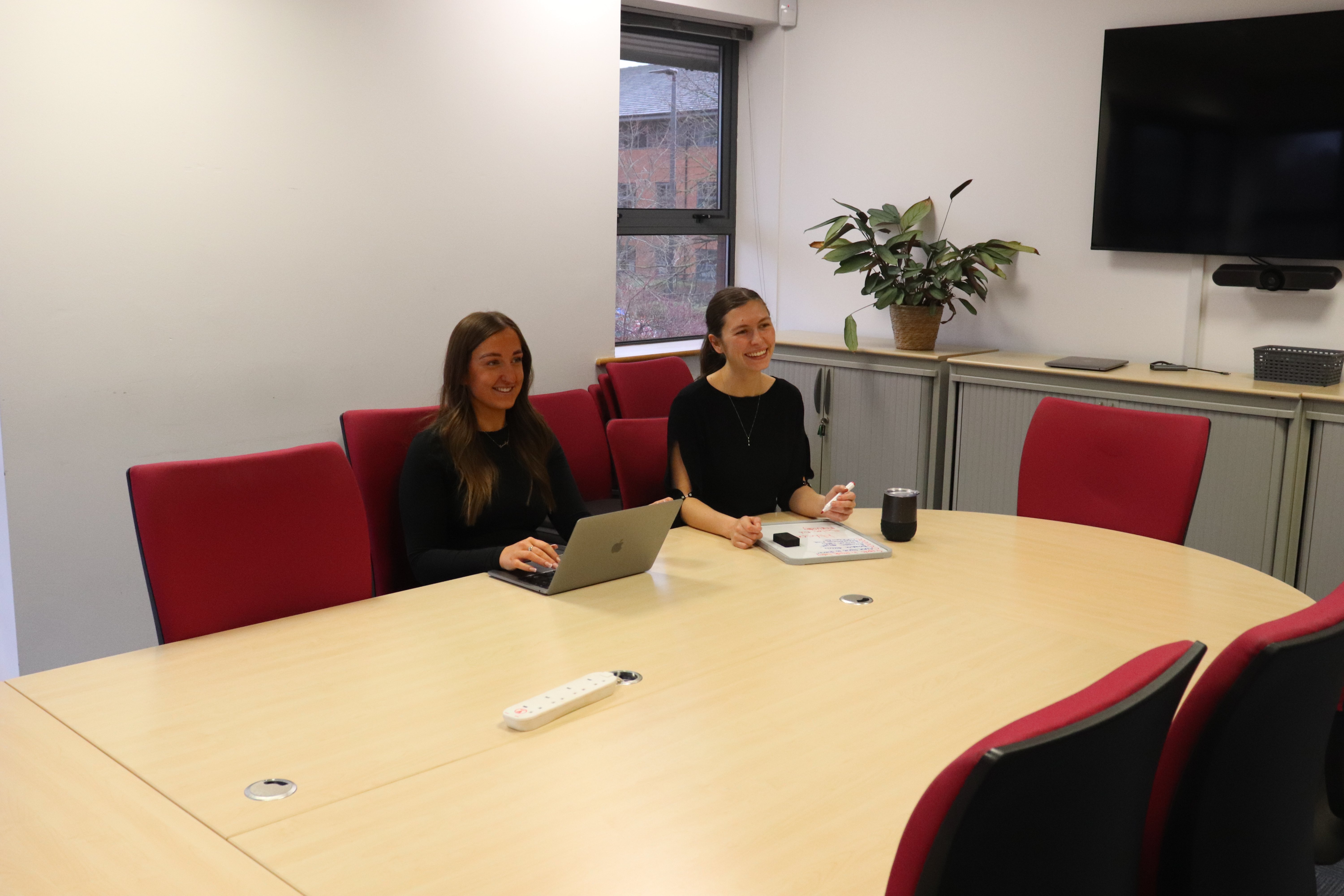 Emily and Sophie with a laptop and notebook both smiling while taking notes during a eeting about ecommerce content marketing.