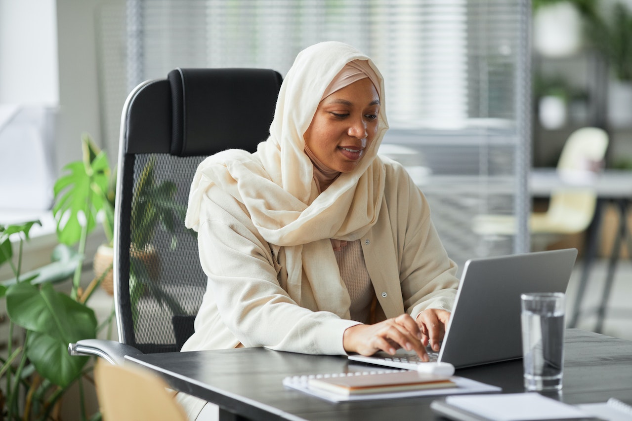 A small business owner in a hijab working at her laptop as she invests in inbound marketing to help grow her business.