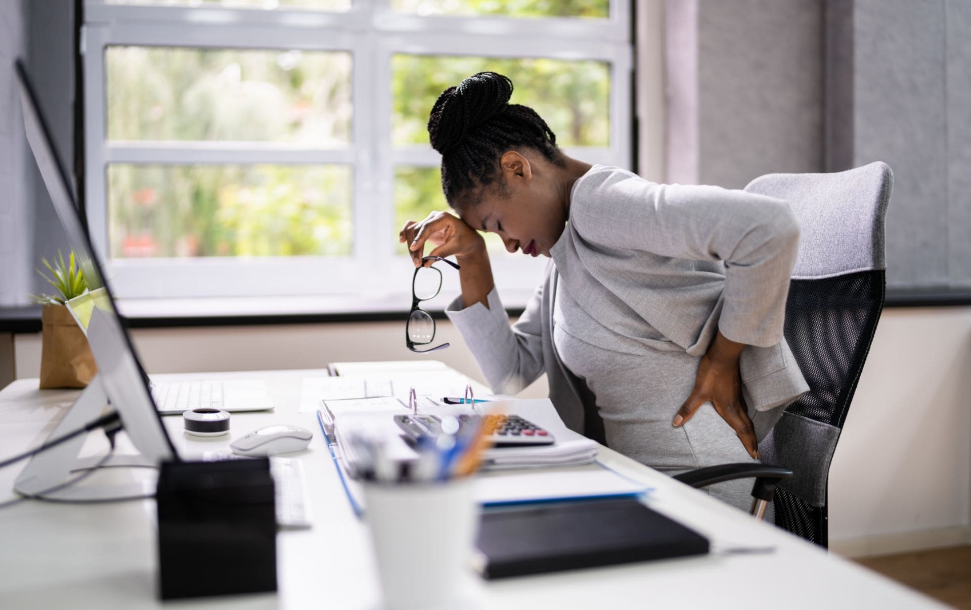 A business woman sitting at her desk with back pain as she leans over her laptop holding her glasses thinking about adopting inbound marketing for her business to help cure her business's growth pains.