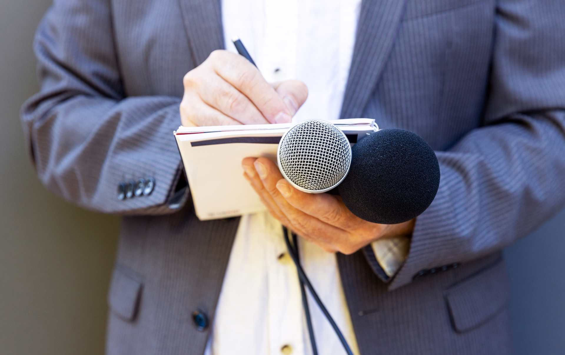 A business owner standing in a suit holding two microphones and writing in a notepad as he decides where to go with inbound or PR for his long term marketing goals