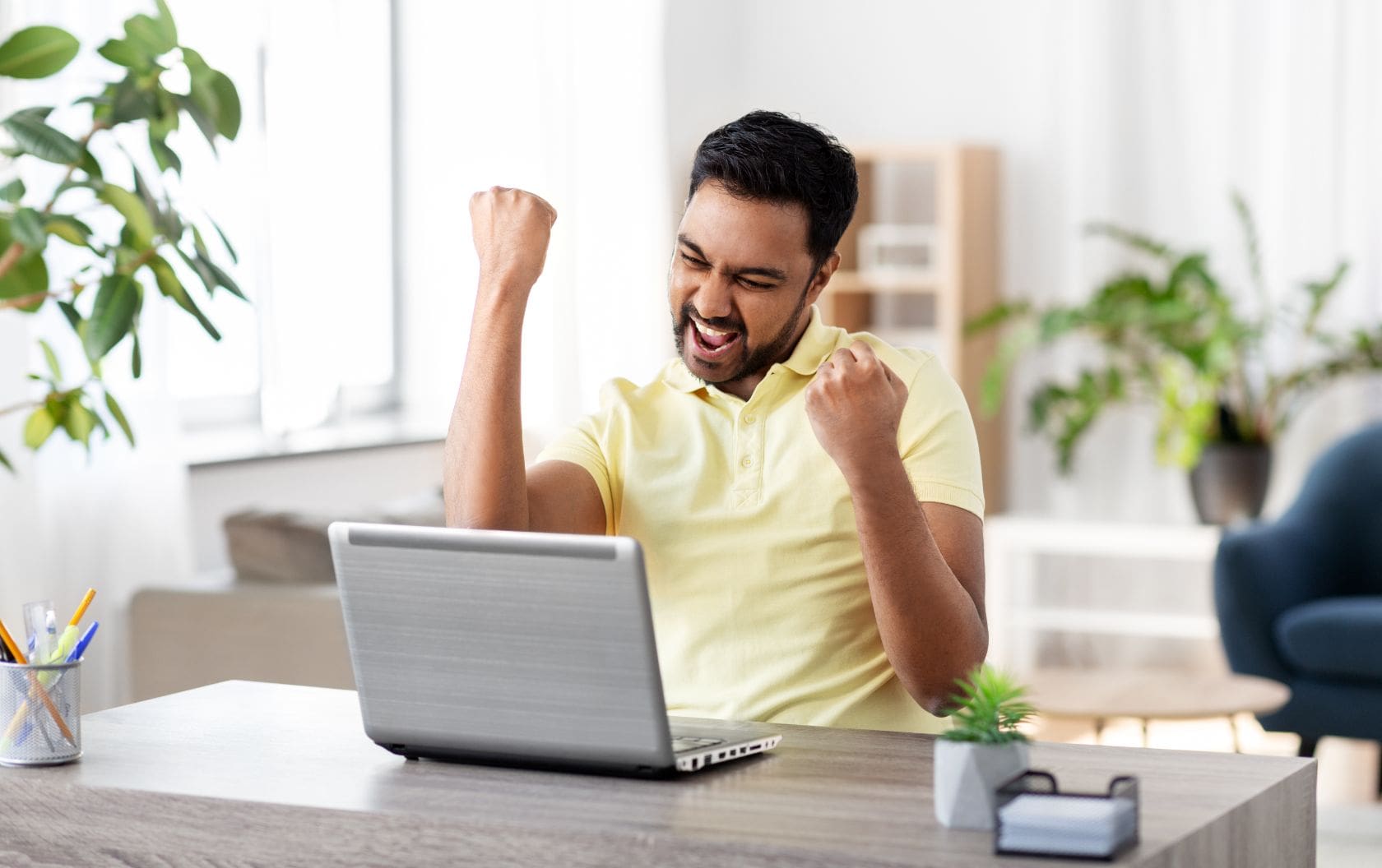 A business man sitting at his kitchen table with his laptop in front of him cheering and punching the air happily as he made another successful sale for his growing small business.