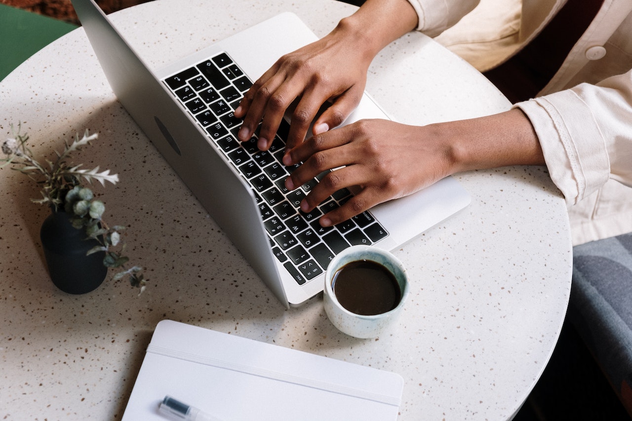 A woman sitting at a table on her laptop researching the Top Website of 2022 winner from The Good Estate with a coffee. 