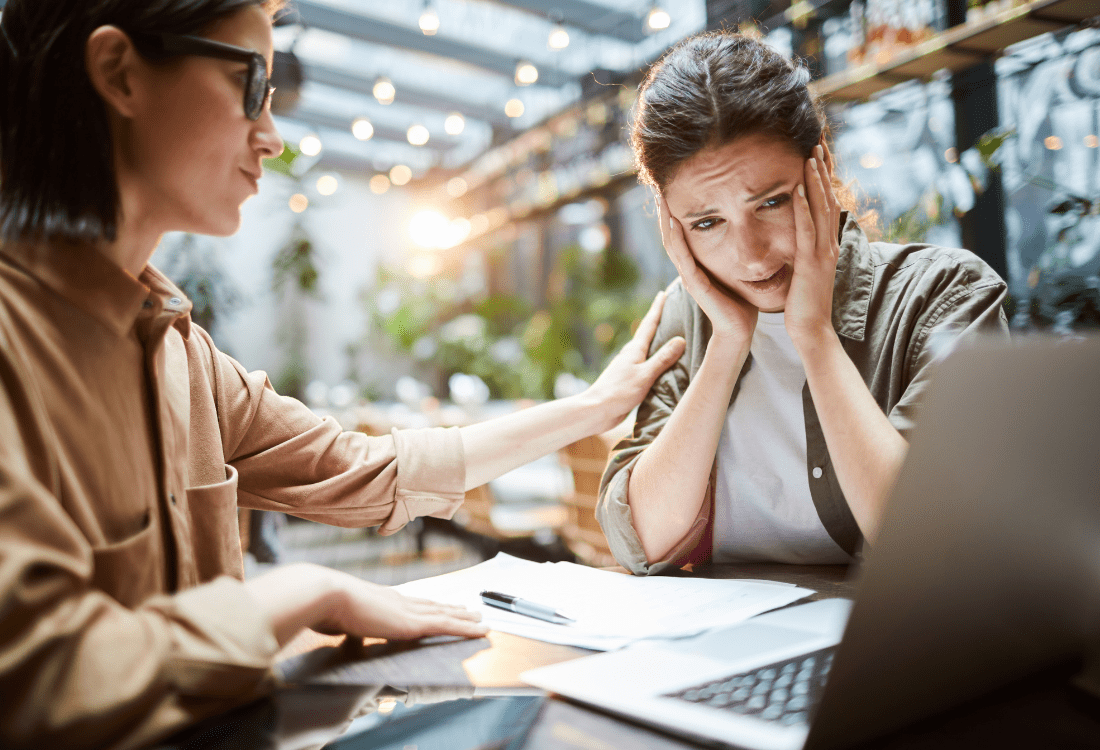 A distraught marketing professional receiving comfort from a colleague after reviewing results of a failed marketing campaign.