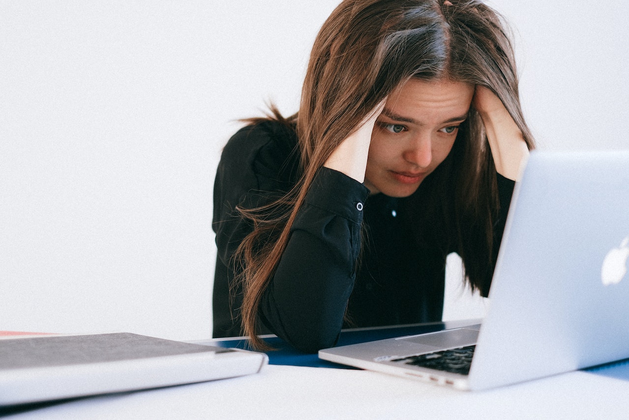 A businesswoman leaning over her laptop with her head in her hands, stressed due to having to manually follow up leads as she doesn't have HubSpot CRM 
