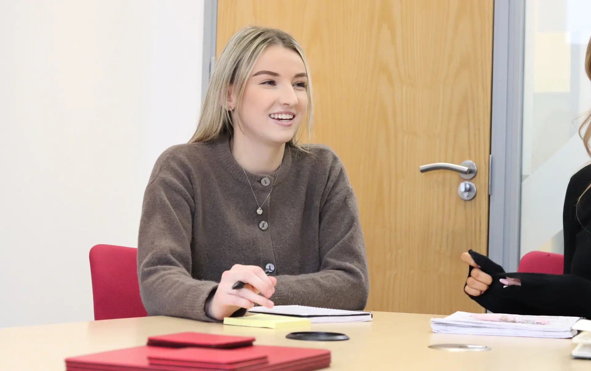 Emily leading a marketing meeting, smiling while taking notes at a conference table during a strategy discussion on SEO and digital visibility.