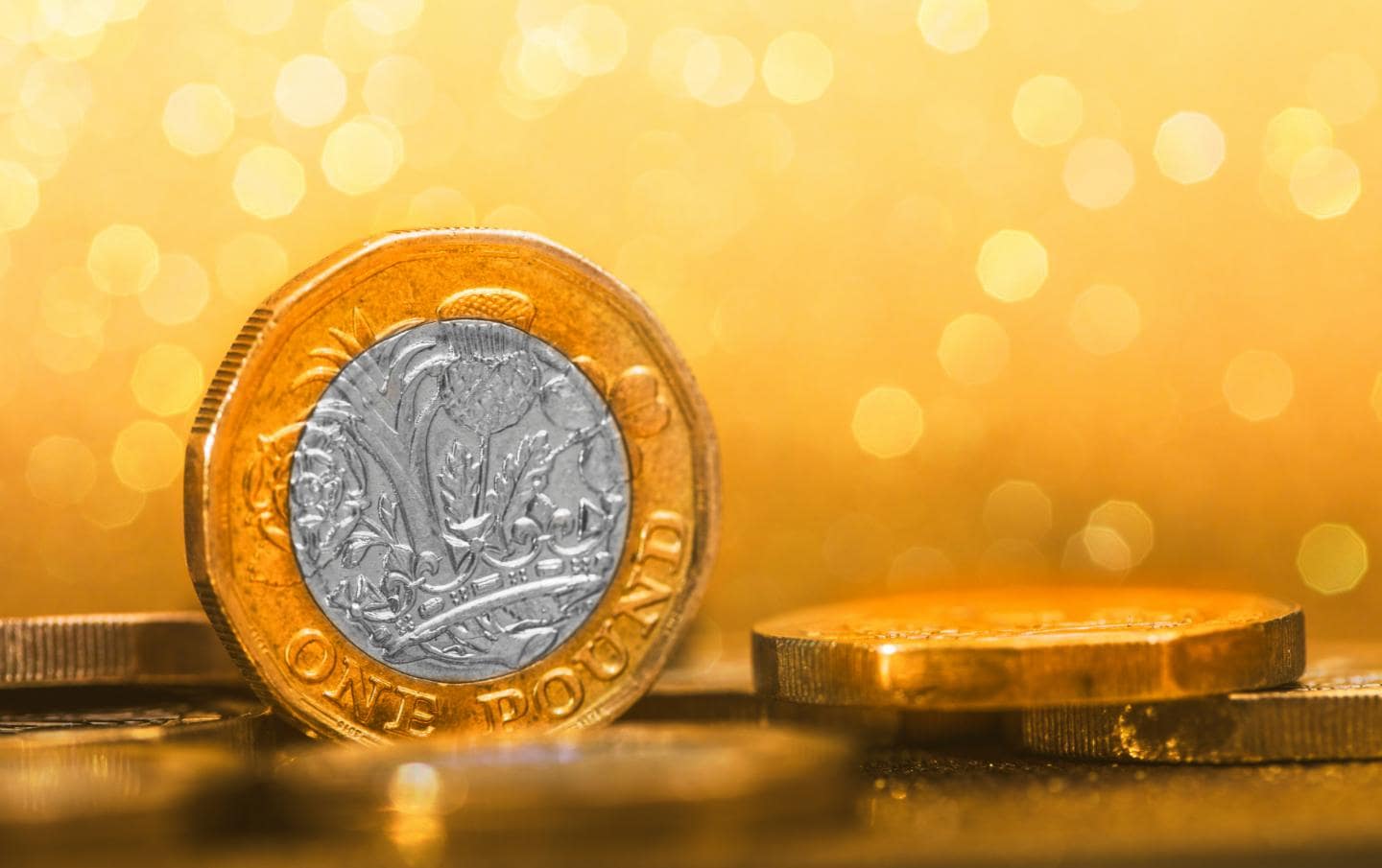 A british pound coin standing upright with stars behind it and four more pound coins laying down around it which are about to be used to invest in a business by a business owner.
