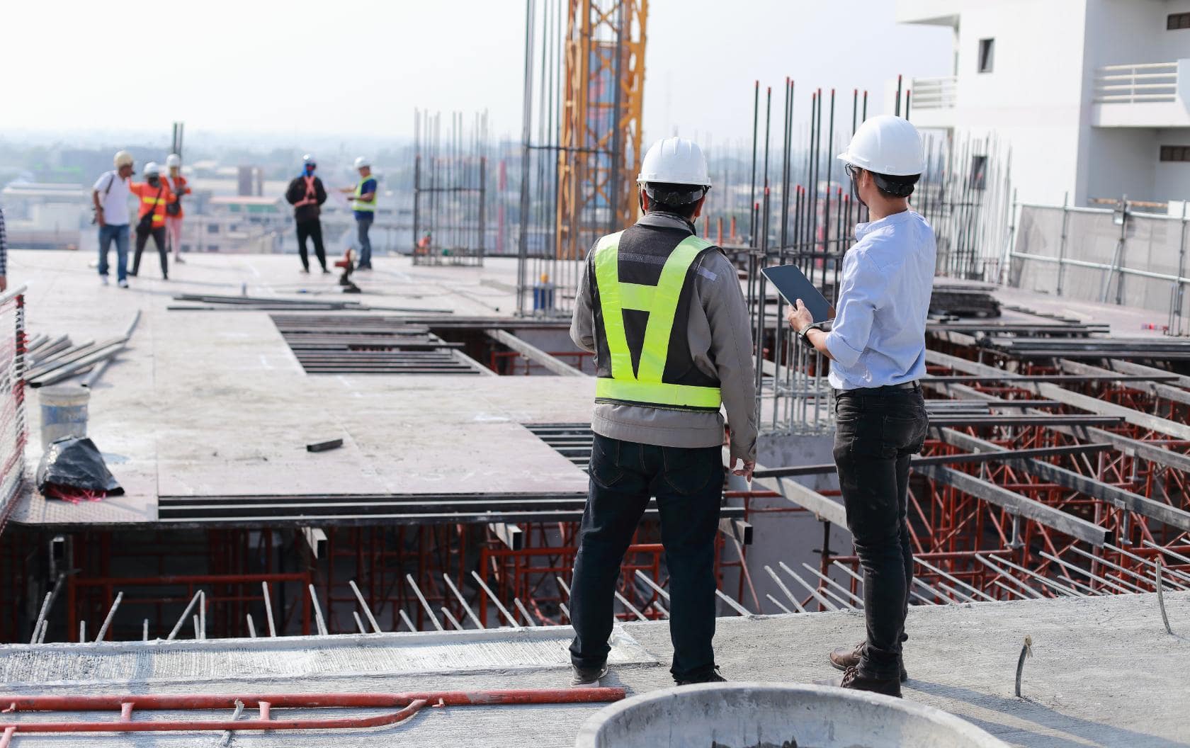 Two construction workers standing, overlooking a the construction of a building with an iPad in one of their hands as they use HubSpot to manage their processes.