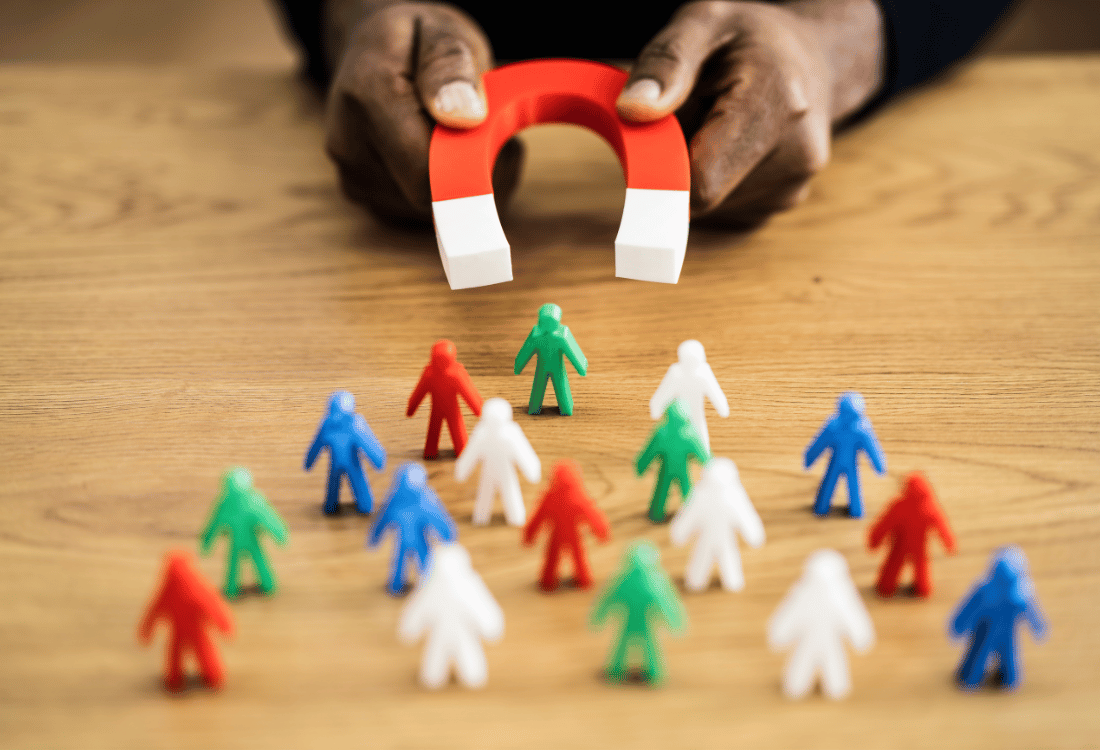 A person using a magnet to attract different coloured small plastic people.