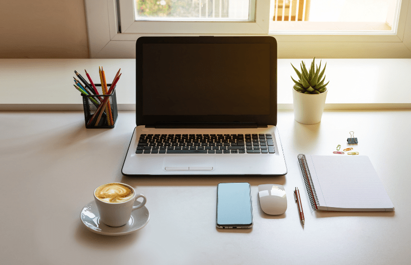 A business owner's desk with all of their paperwork, stationary, post its and glasses pushed to the top of their desk and their Macbook closest to them at the bottom of the desk as they start a more organised marketing strategy 