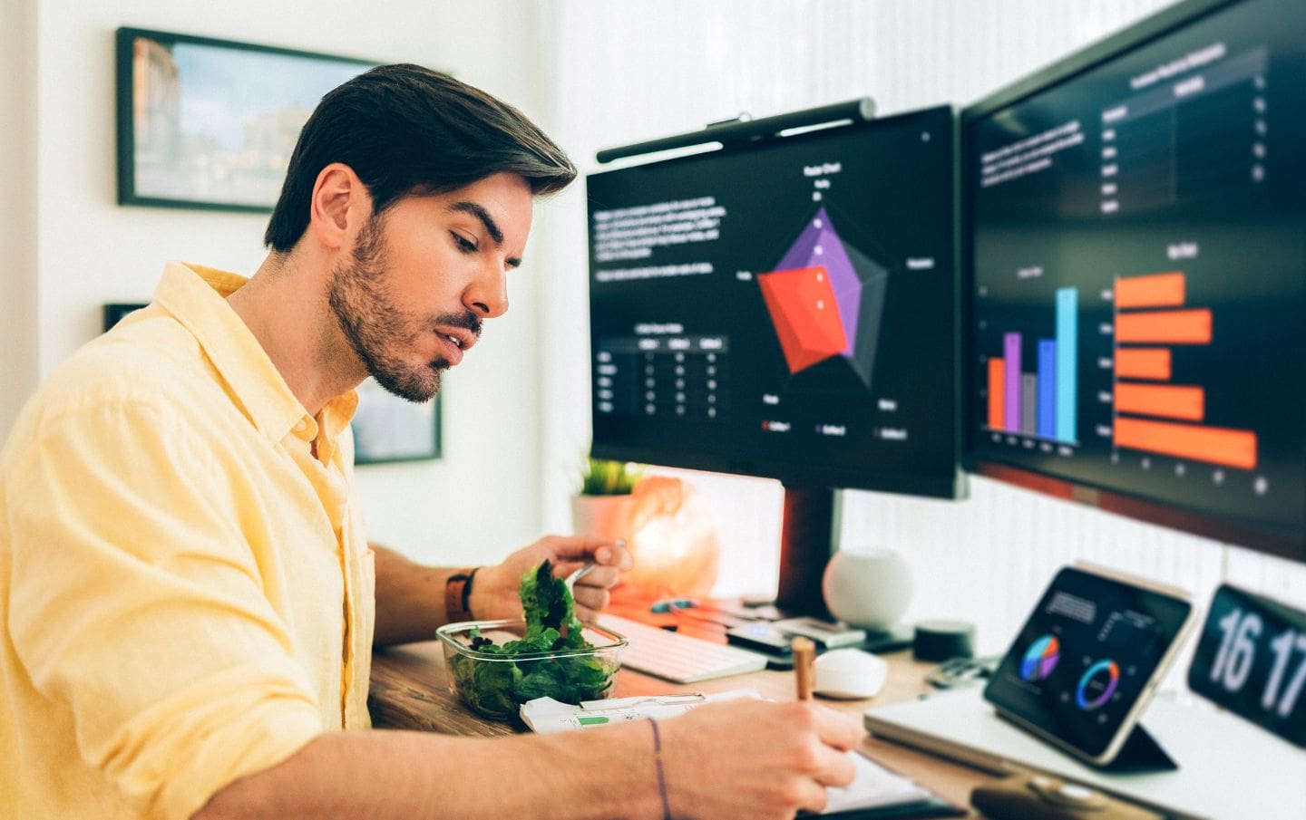 A business owner creating a report of his sales results which have increased due to him using HubSpot CRM for his business, by viewing them on his three desktop screens at his desk