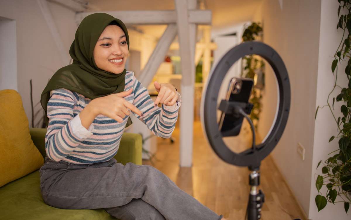 A social media influencer sitting on her sofa in front of a phone and ring light telling her audience on TikTok to check the link in the description after being sponsored by an SME through Influencer Marketing