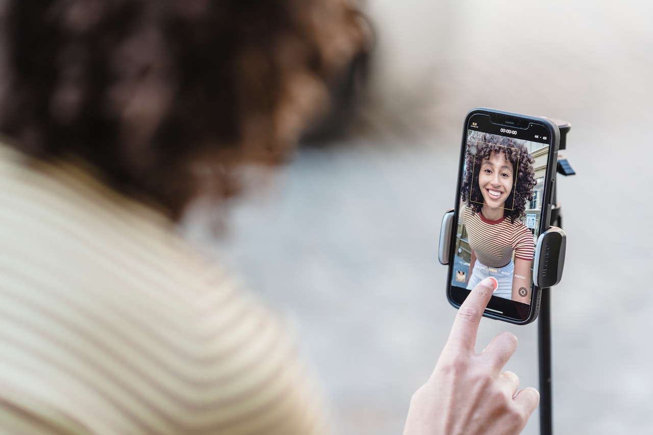 a woman smiling into her smartphone screen which is on a tripod ready to create video marketing content for her business