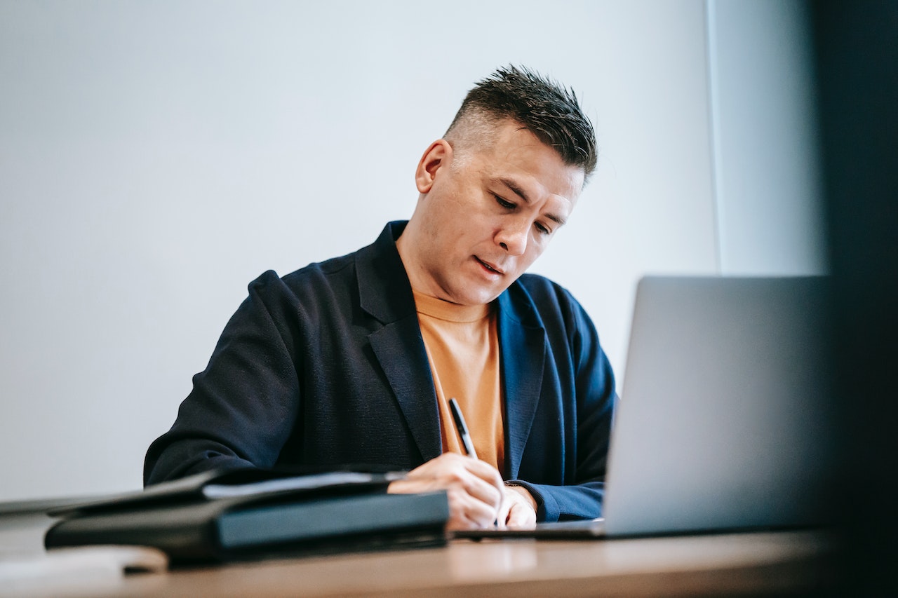 A business man sitting at his desk with a laptop and two notebooks replying to negative reviews effectively to help grow his business