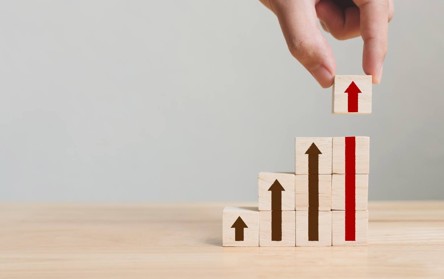 A business owner stacking four columns of wooden building blocks each column with an arrow pointing higher and higher upward as the business owner's S M E grows from using HubSpot