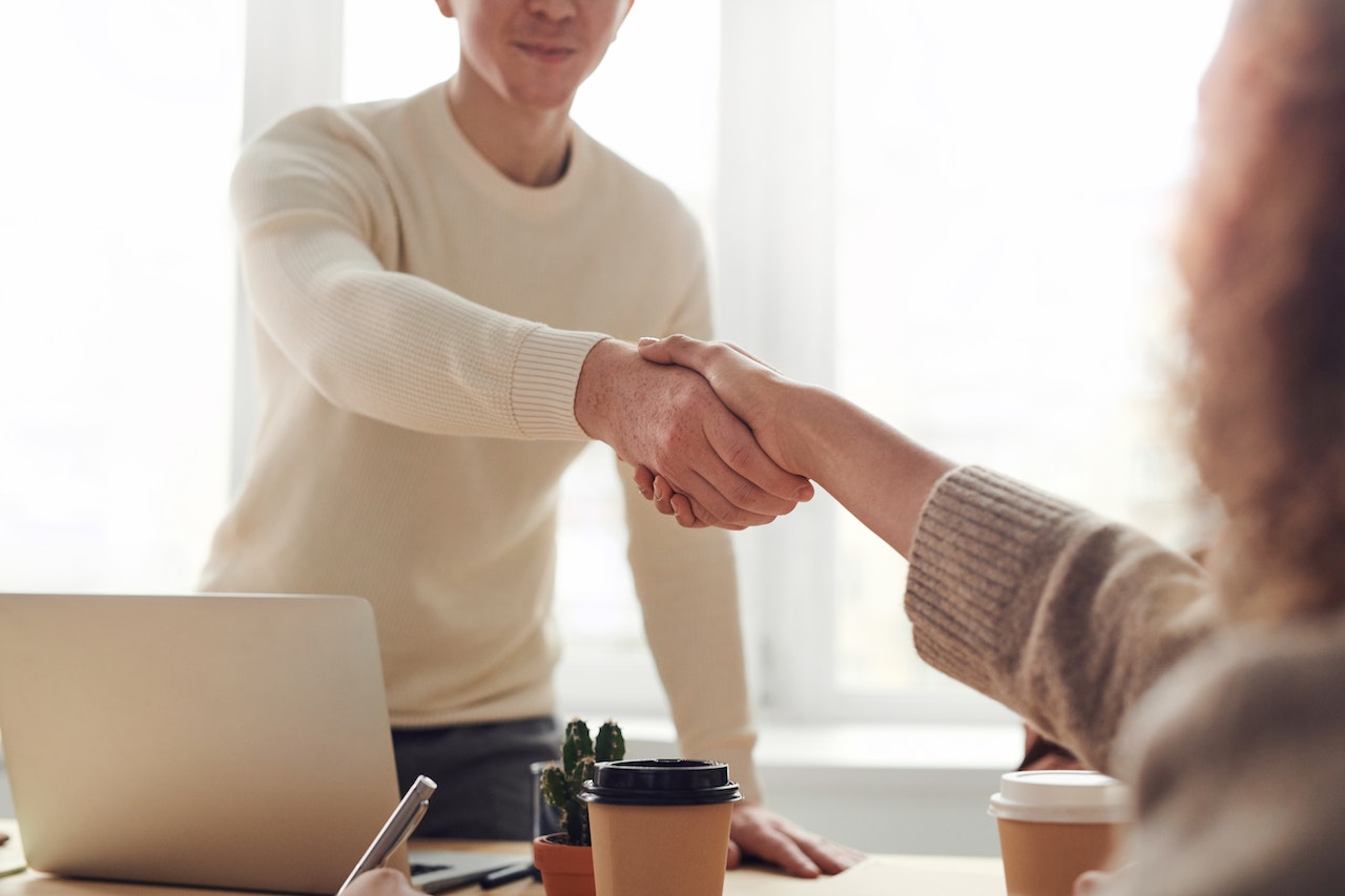 A small business owner shaking hands across the table with one of their customers who is a strong advocate for the business both with a cup of coffee each