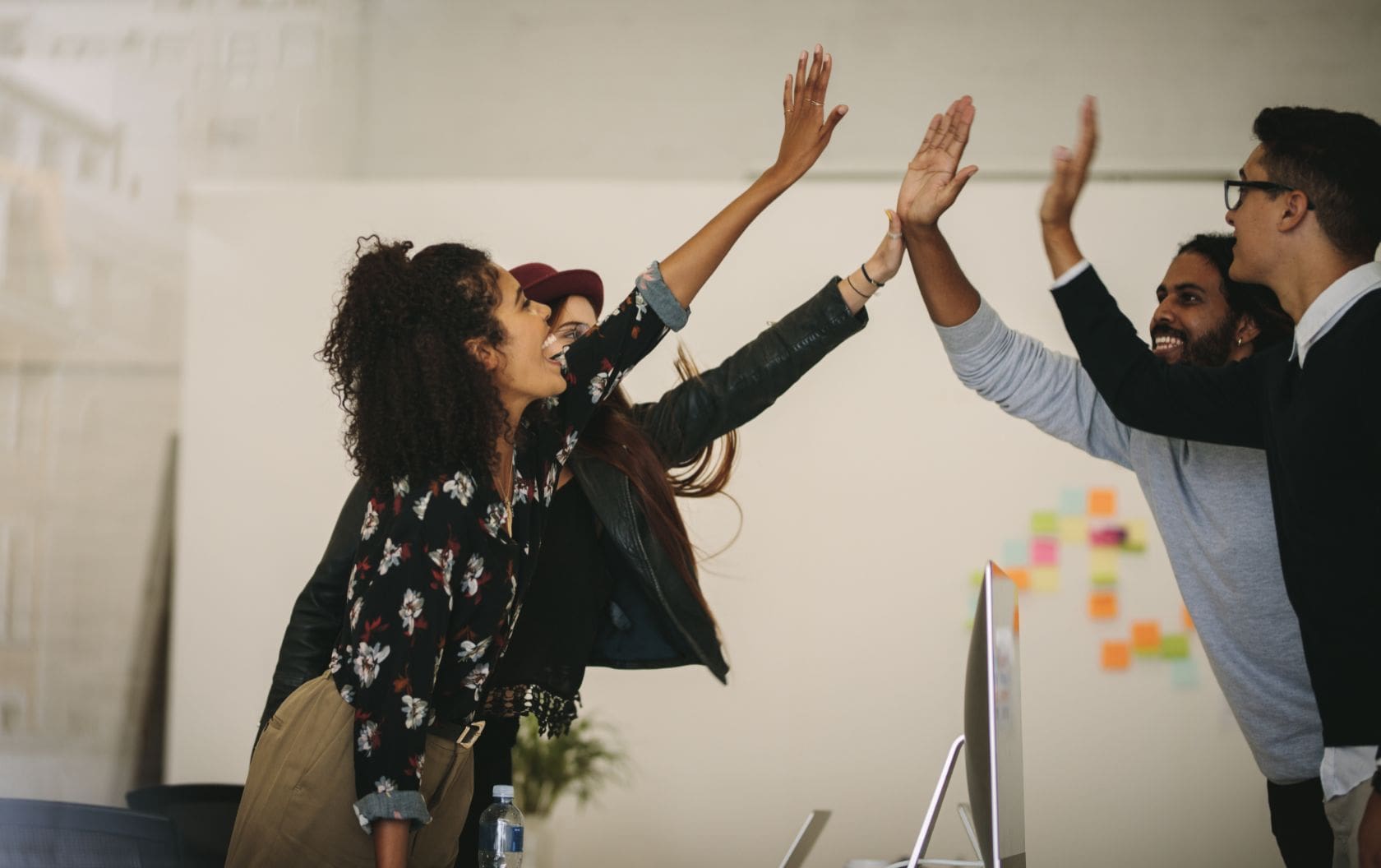 Two woman and two men in a business's marketing team high-fiving over the desk as they find that their inbound marketing strategy is creating efficient business growth.