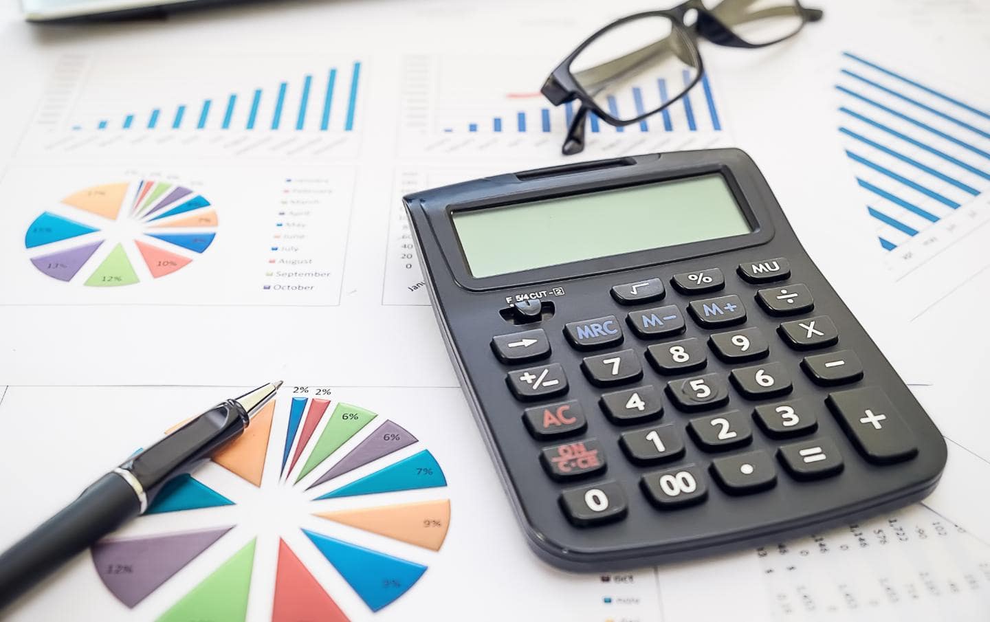 Budgeting charts on multiple pieces of paper scattered over a desk with a calculator, pen and glasses resting on the papers belonging to a business owner who is getting the most out of their marketing budget this year 