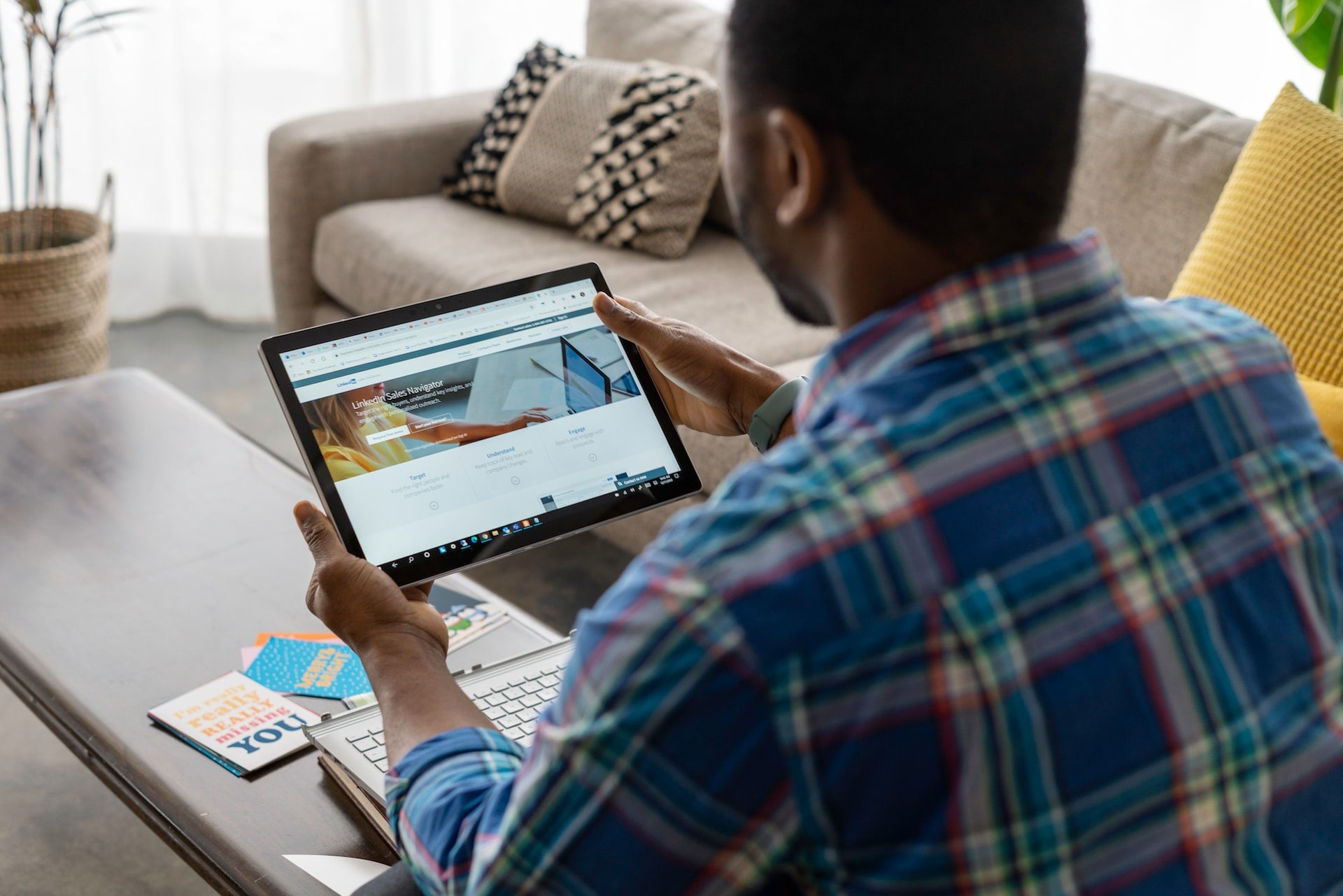 A business owner sitting on his sofa looking at LinkedIn on his tablet to check his business company profile and personal profile