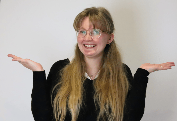 Emma from the JDR Group smiling with her hands raised in a playful shrug against a plain background.