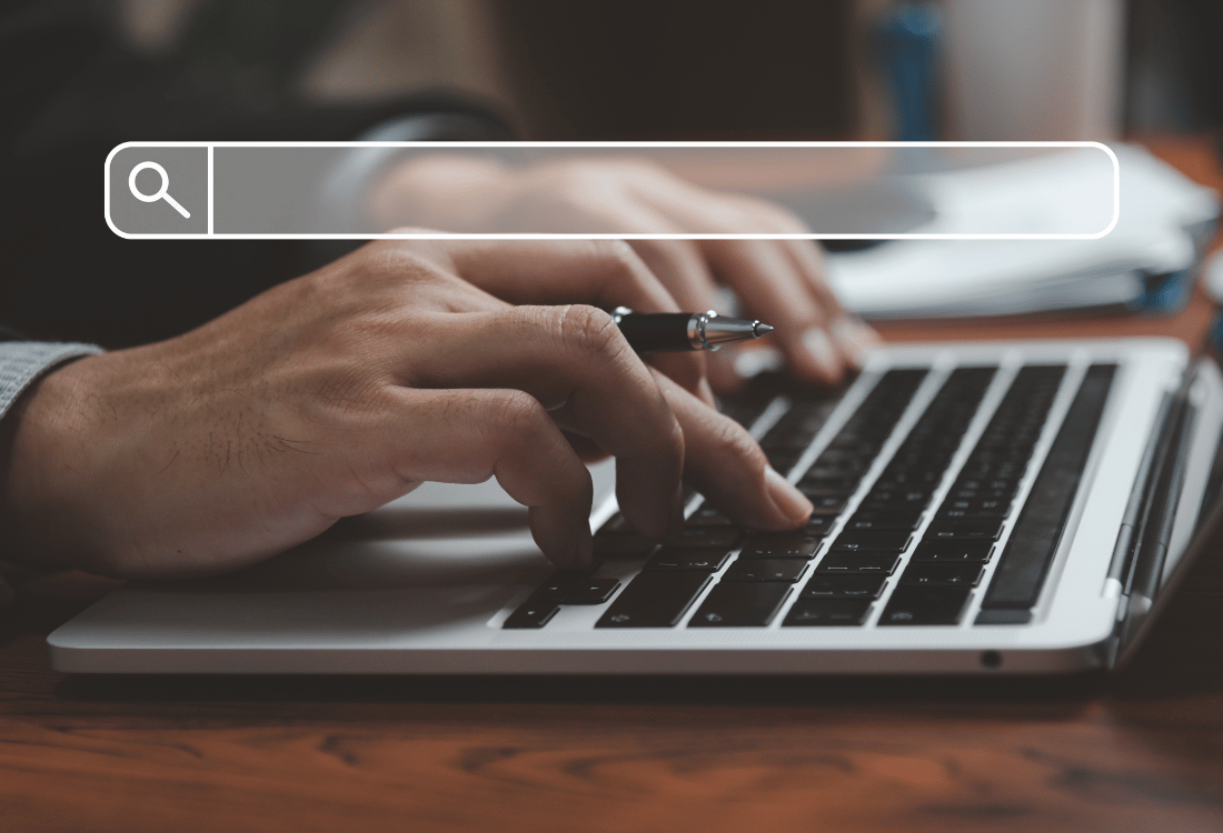 Close-up of hands typing on a laptop keyboard with a search bar overlay at the top of the image. The background is slightly blurred, focusing on the hands and the laptop.
